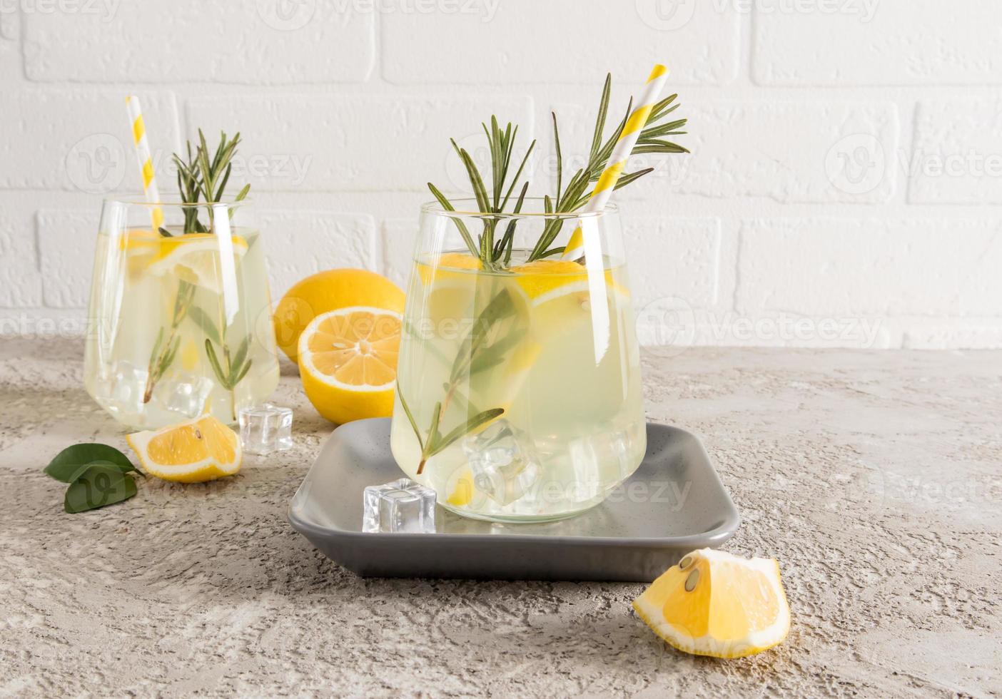 a glass of homemade lemonade with ice cubes on a ceramic plate and a concrete gray table. delicious summer drink without preservatives and dyes. photo