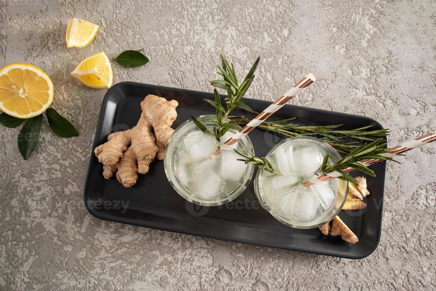 top view of two glasses of ginger lemonade, pieces of ice and sprigs of rosemary. a healthy chilled drink in the heat. photo