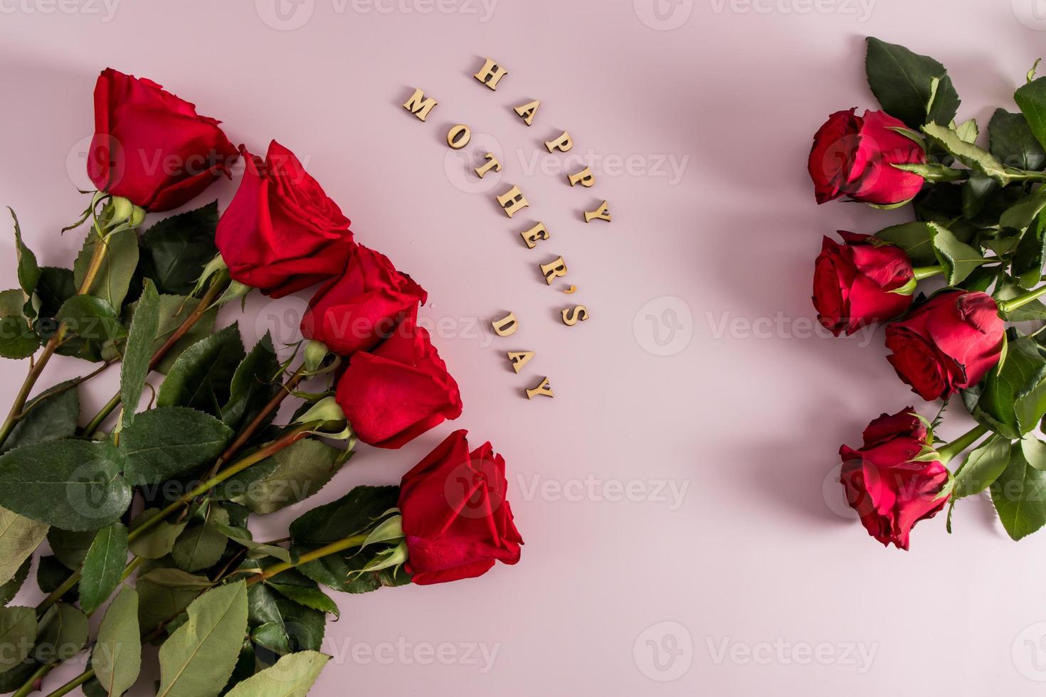 a festive composition of red roses on a pink background with the inscription in wooden letters - happy mother's day. top view. flat styling. photo