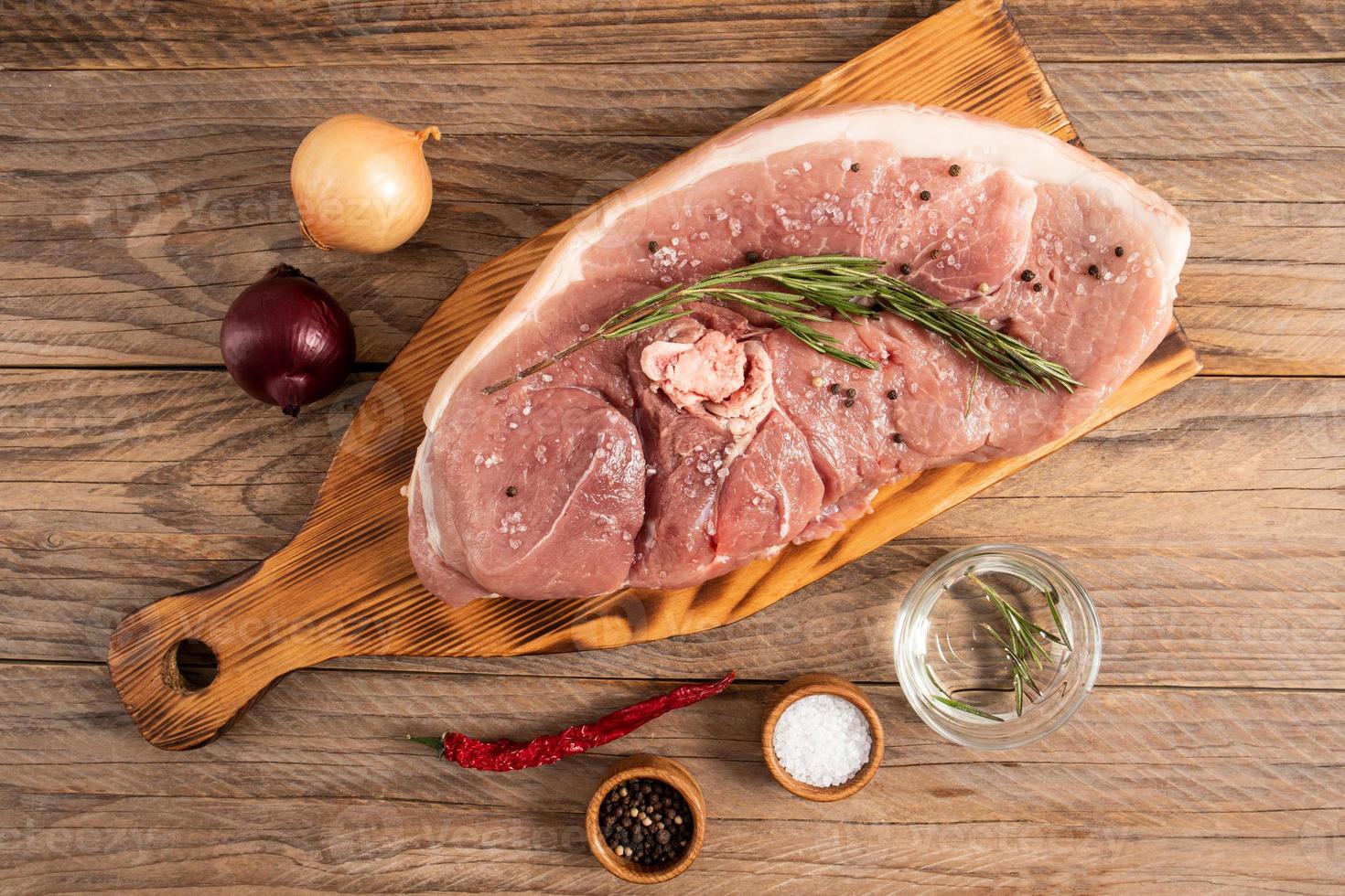 a large raw piece of steamed pork meat on a cutting board and a wooden table with spices. top view. rustic style. photo