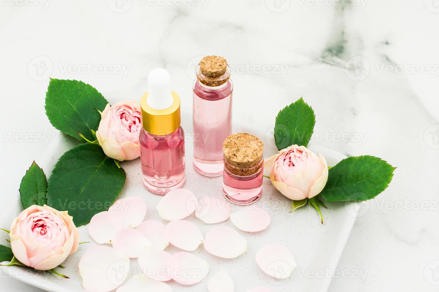 bottles of essential, cosmetic rose oil on a ceramic tray with rose petals and buds. the concept of skin care, beauty, well-being. photo