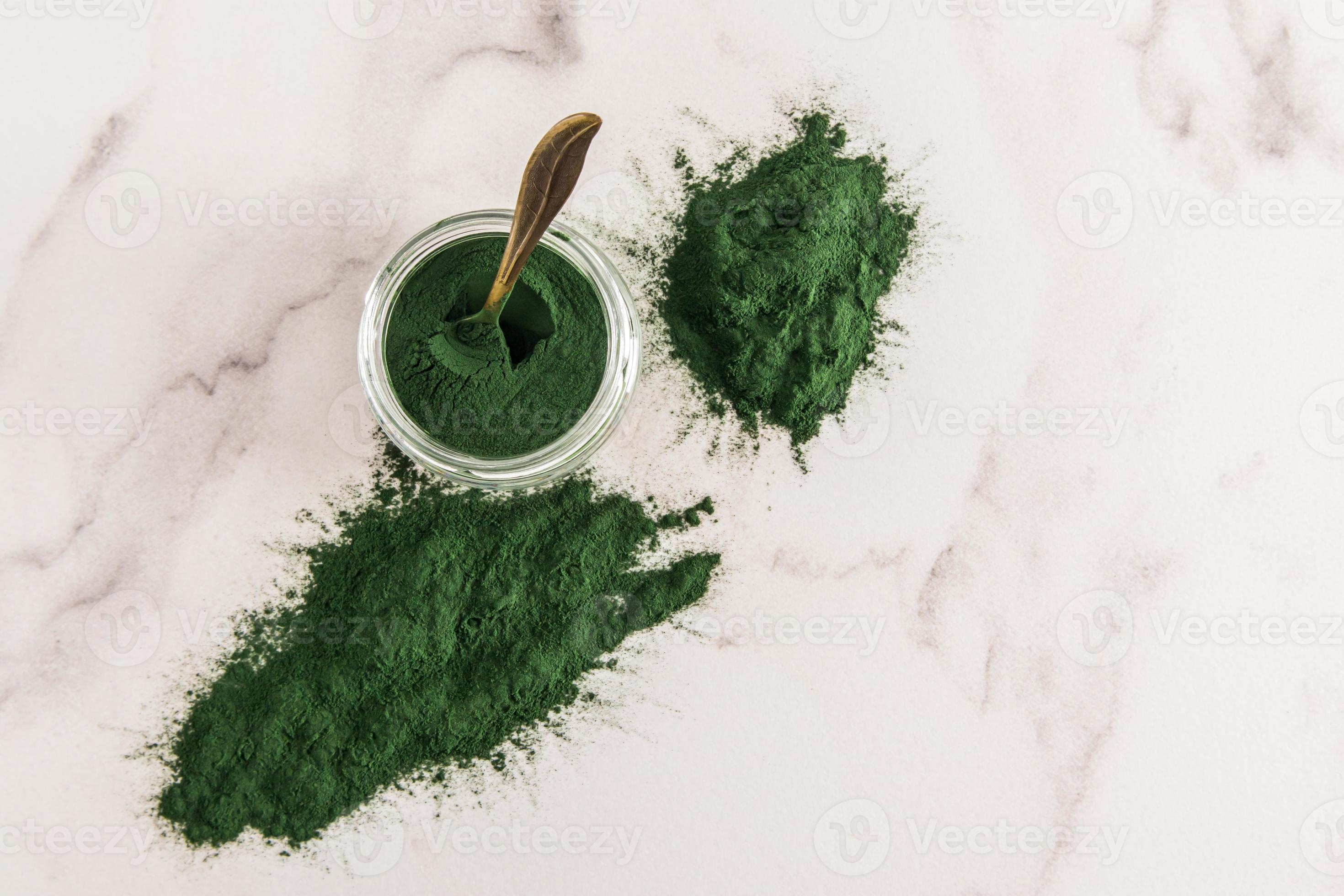 scattered spirulina powder on a marble white background and a glass jar