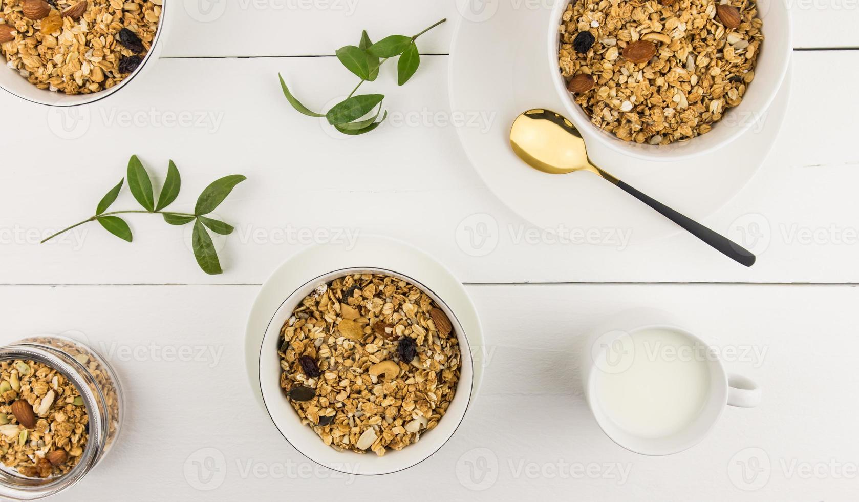 top view of bowls with homemade muesli or granola made of oatmeal, raisins, nuts with a mug of fresh milk. healthy eating. photo