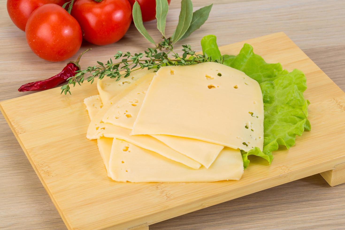 queso cheddar en rodajas sobre tablero de madera y fondo de madera foto