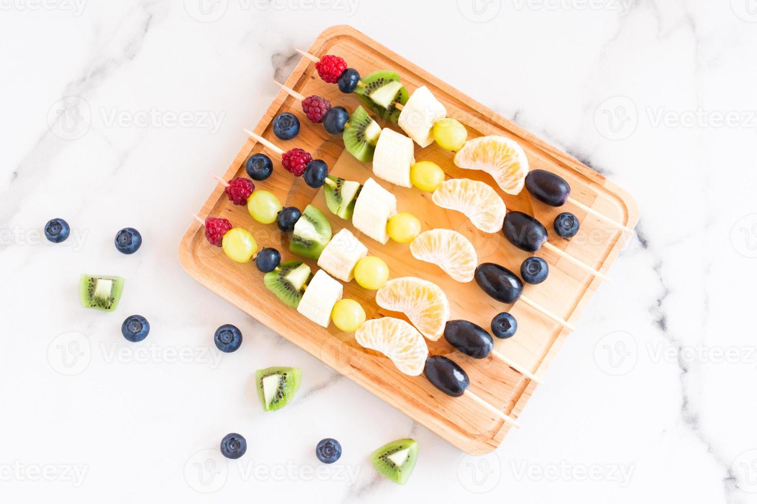 Fruit canapes on a wooden board.delicious and healthy food.mix of tangerine, kiwi, banana, grapes.view from above. photo