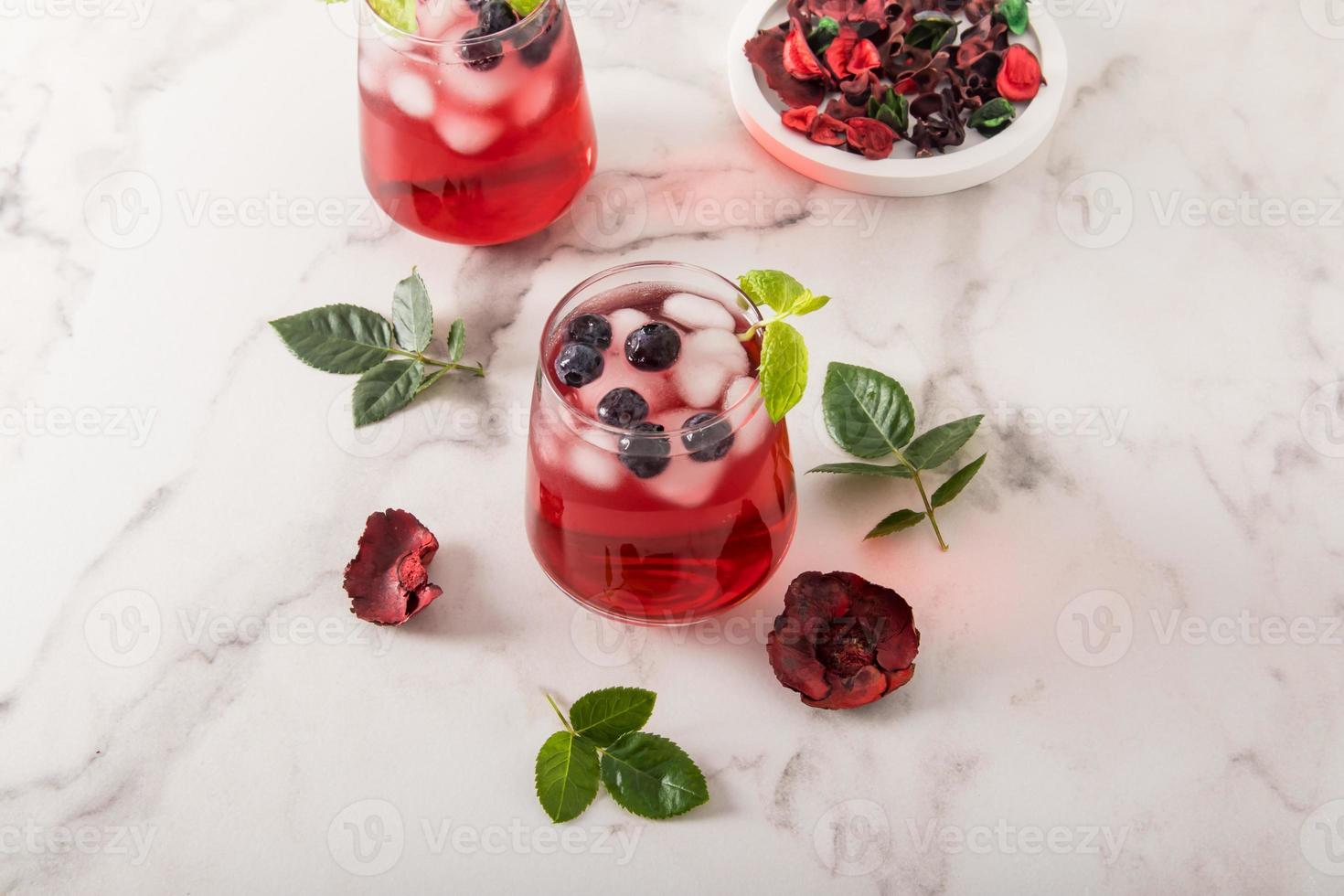 tonic vitamin drink from rose petals hibiscus with blueberries, mint leaves, ice cubes in glasses on a marble table. iced tea. photo