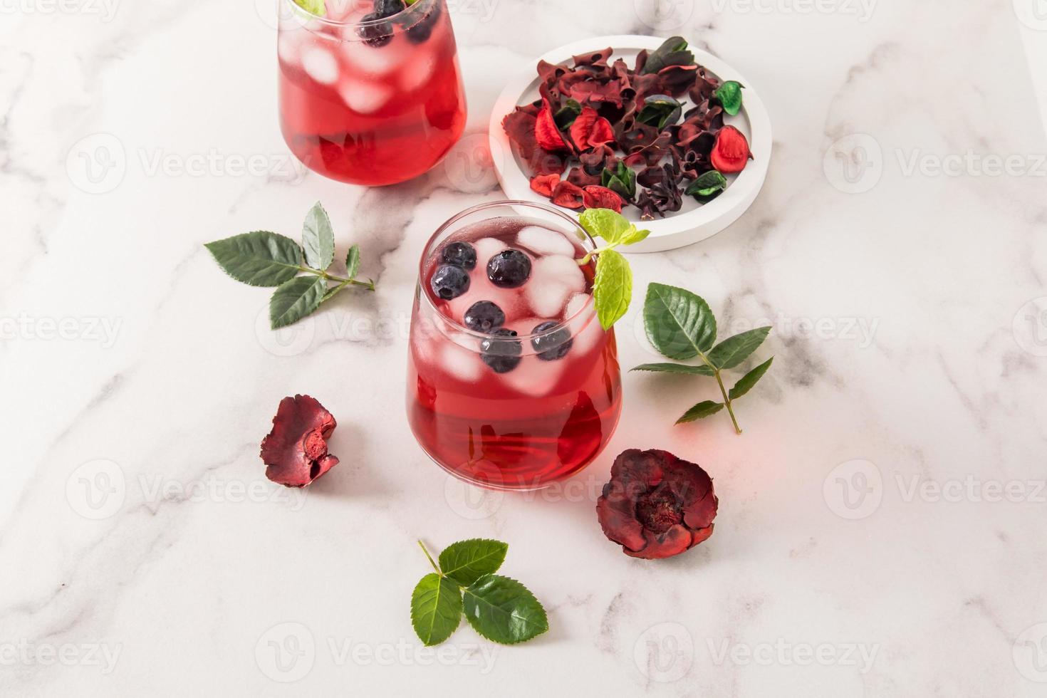 tonic vitamin drink from rose petals hibiscus with blueberries, mint leaves, ice cubes in glasses on a marble table. iced tea. photo