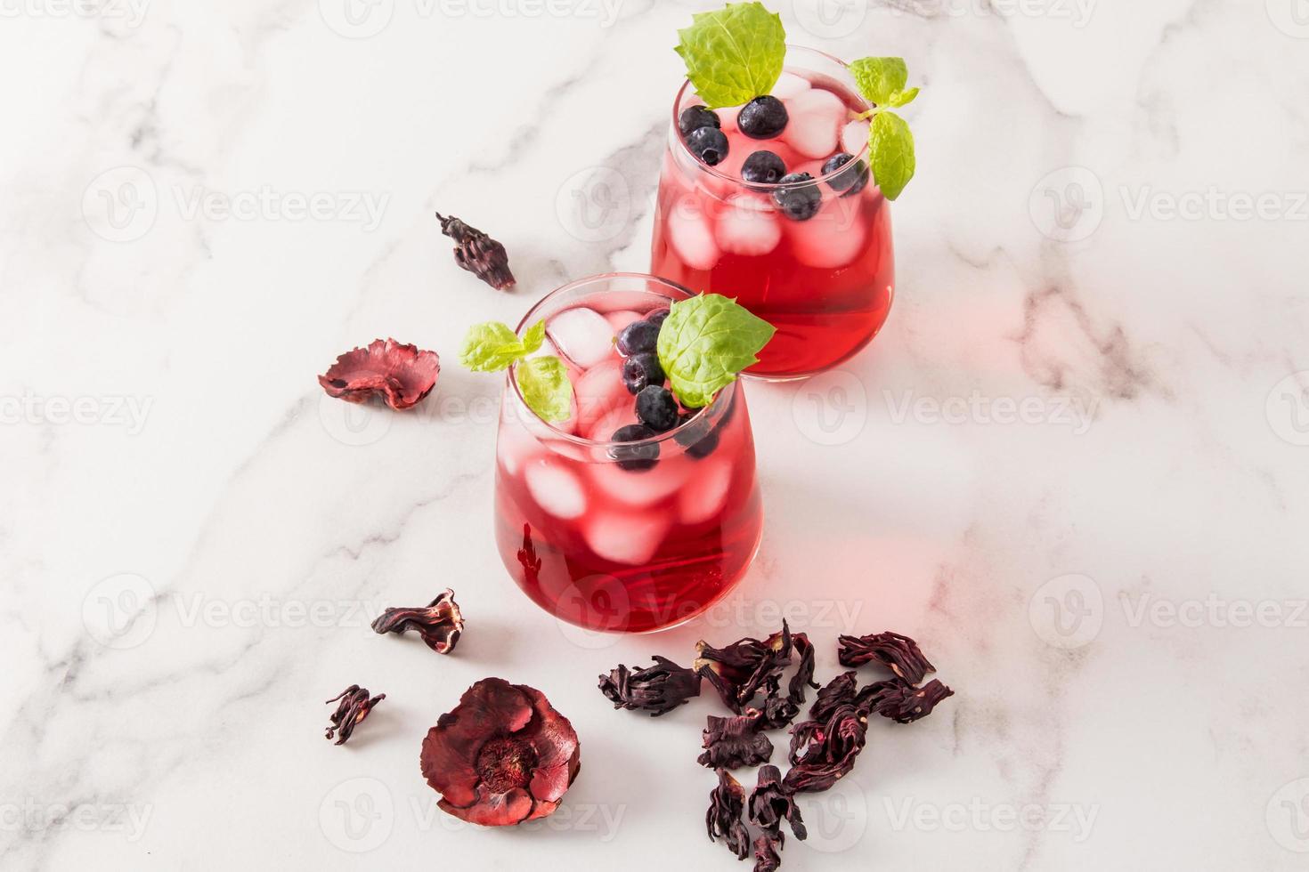 two glass glasses with cold hibiscus tea, blueberries, lime slices and ice cubes on a marble table. high content of vitamins, antioxidants. photo
