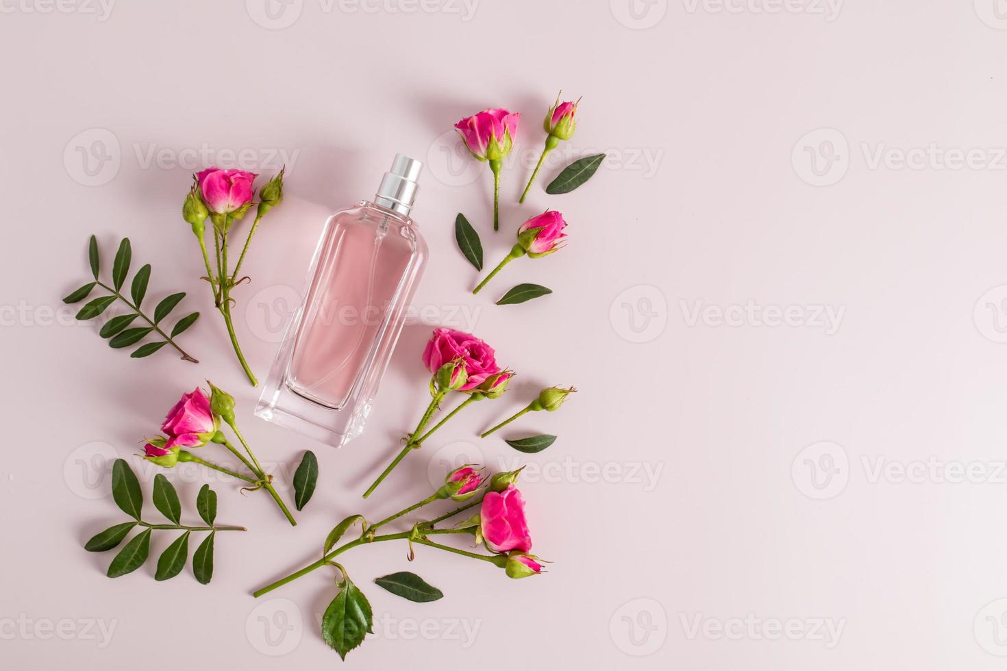 perfume en una botella de vidrio sobre un fondo rosa con capullos de rosas frescas. vista superior. una copia del espacio. diseño de plantilla. foto
