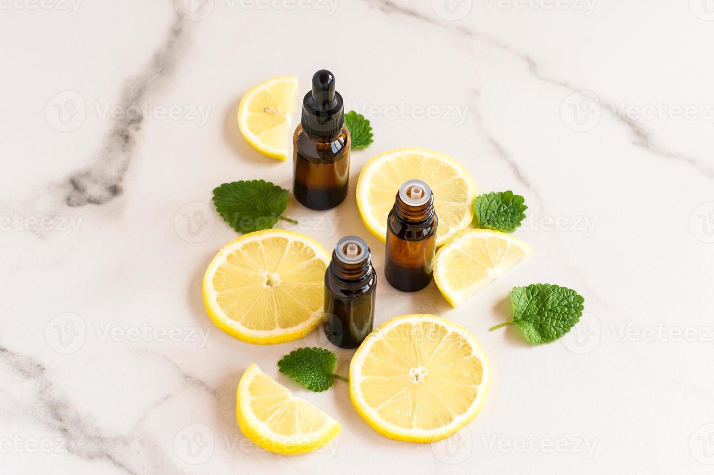 cosmetic bottles of dark glass with essential oils of lemon and lemon balm leaves on a marble table. photo