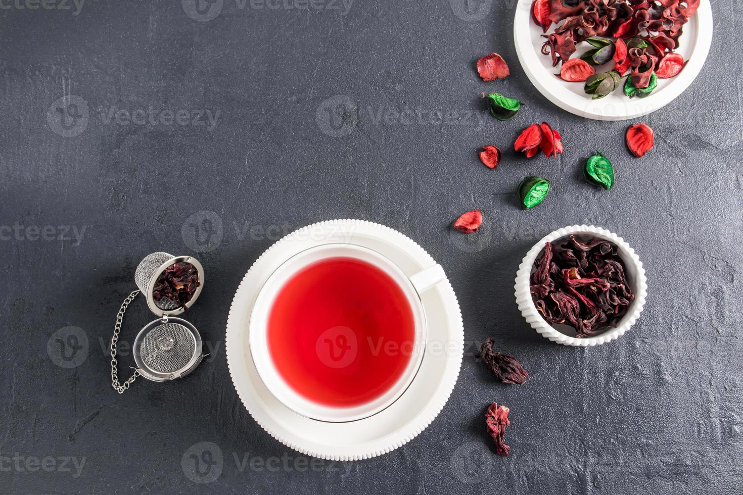 top view of a white cup with a saucer of fragrant hibiscus rose tea. dry rose leaves in the bowl. black background. natural antiseptic, vitamins. photo