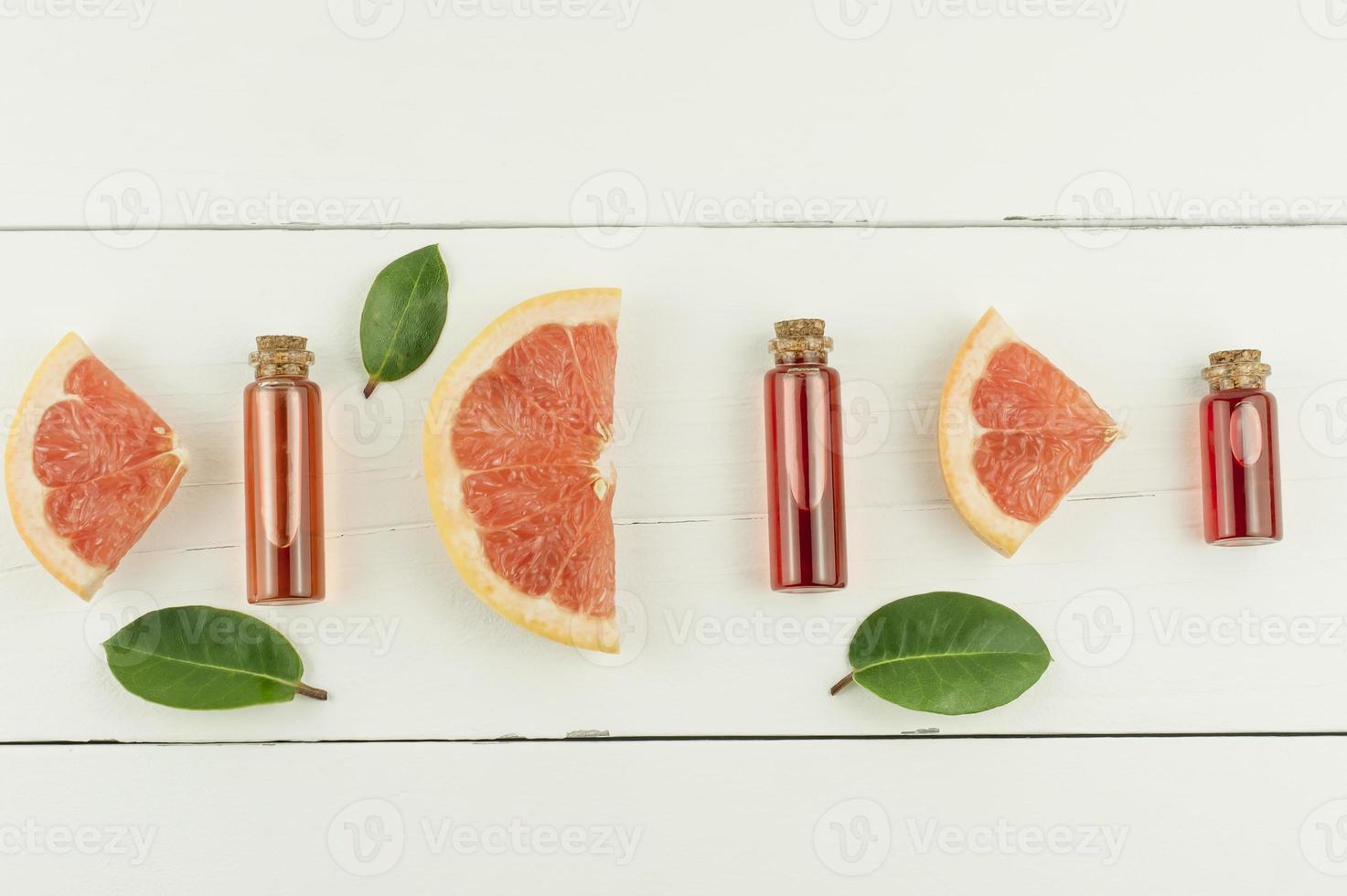 top view of bottles with a lid with grapefruit essential oil or cosmetic essence and fruit and green leaf slates. flat lay . white background. photo
