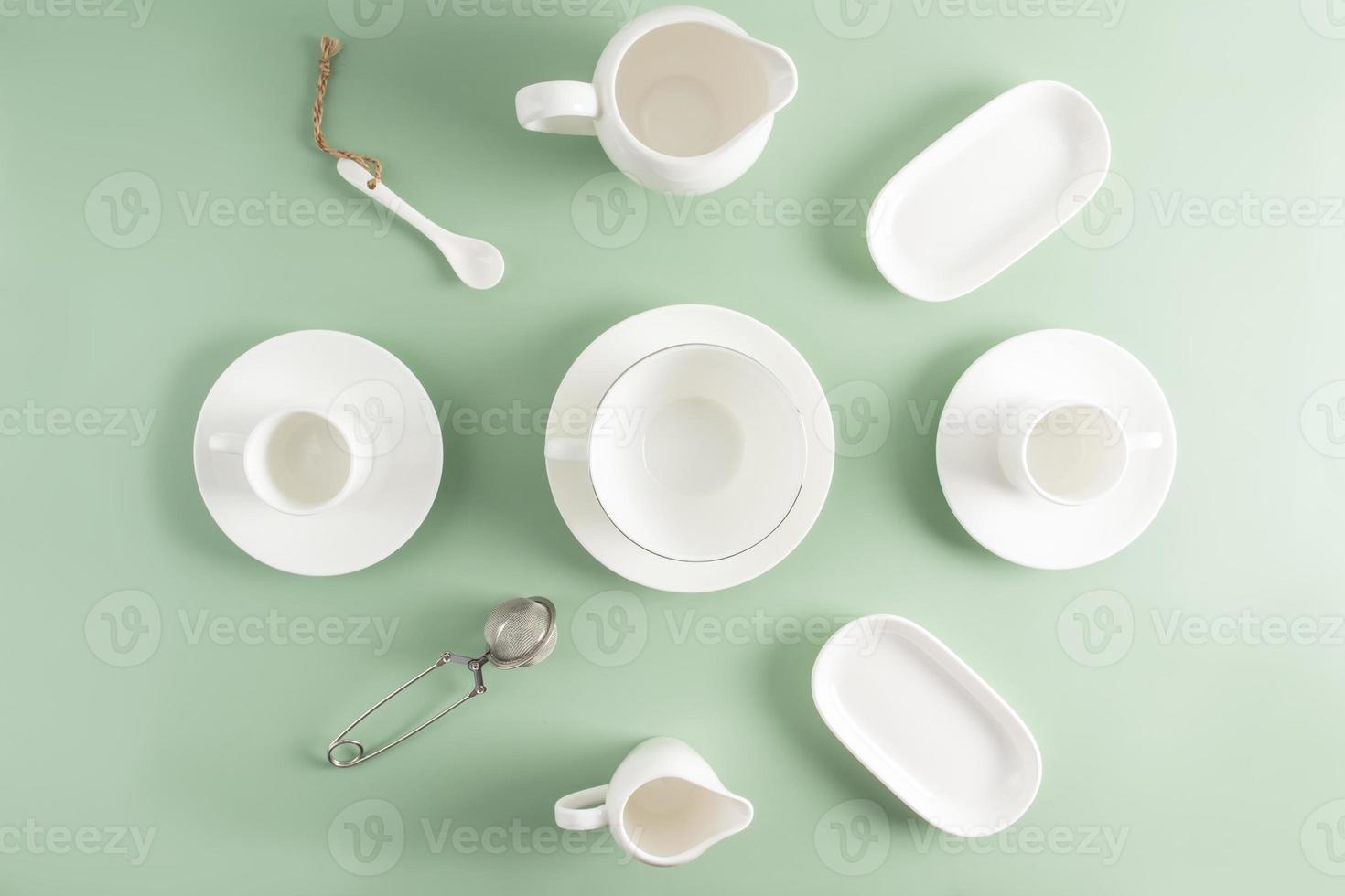 tazas de cerámica blanca y porcelana, platillos, jarra de leche de diferentes formas sobre un fondo verde claro. vista superior. endecha plana foto