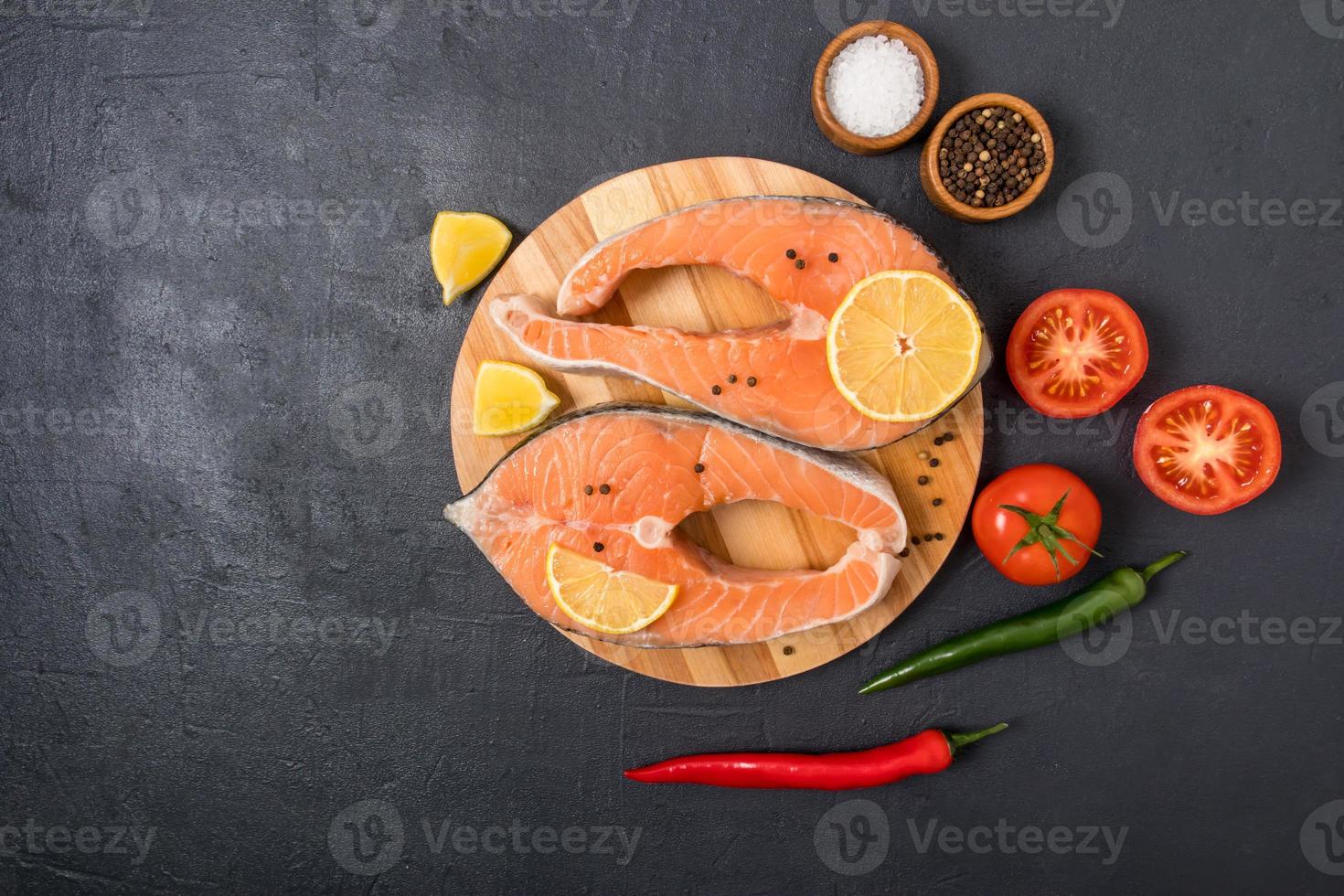 top view of two fresh salmon steaks on a round wooden board with lemon, pepper and tomatoes. the concept of healthy eating, cooking healthy food. photo