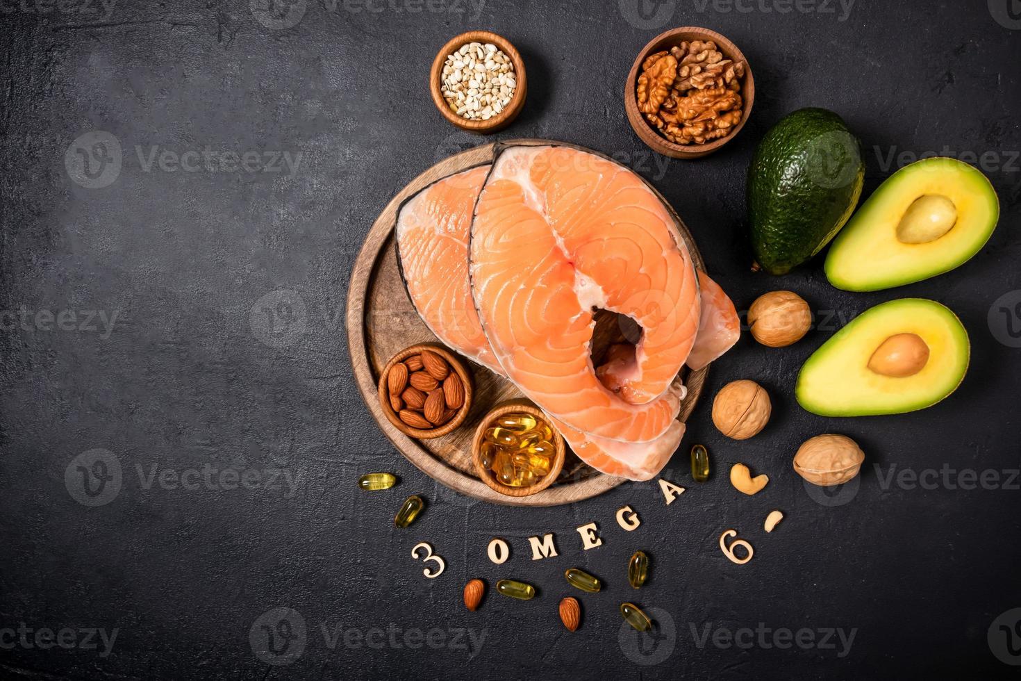 two raw salmon steaks on a round wooden tray surrounded by ripe avocado, nuts, seeds, omega3 capsules. top view. copy of the space. photo