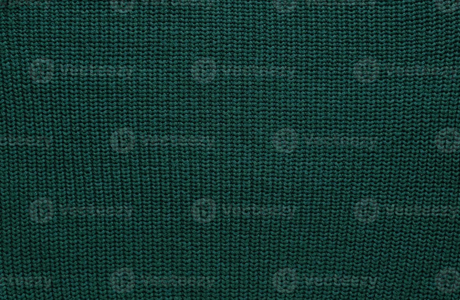 Texture of smooth knitted dark green sweater with pattern. Top view, close-up. Handmade knitting wool or cotton fabric texture. Background of Large Ribs knit pattern with knitting needles or crochet. photo