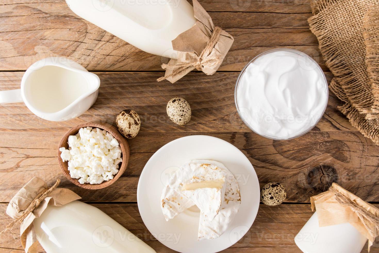 background with dairy products. top view of the wooden countertop with bottles of milk, bowls of cottage cheese, eggs, cheese. photo