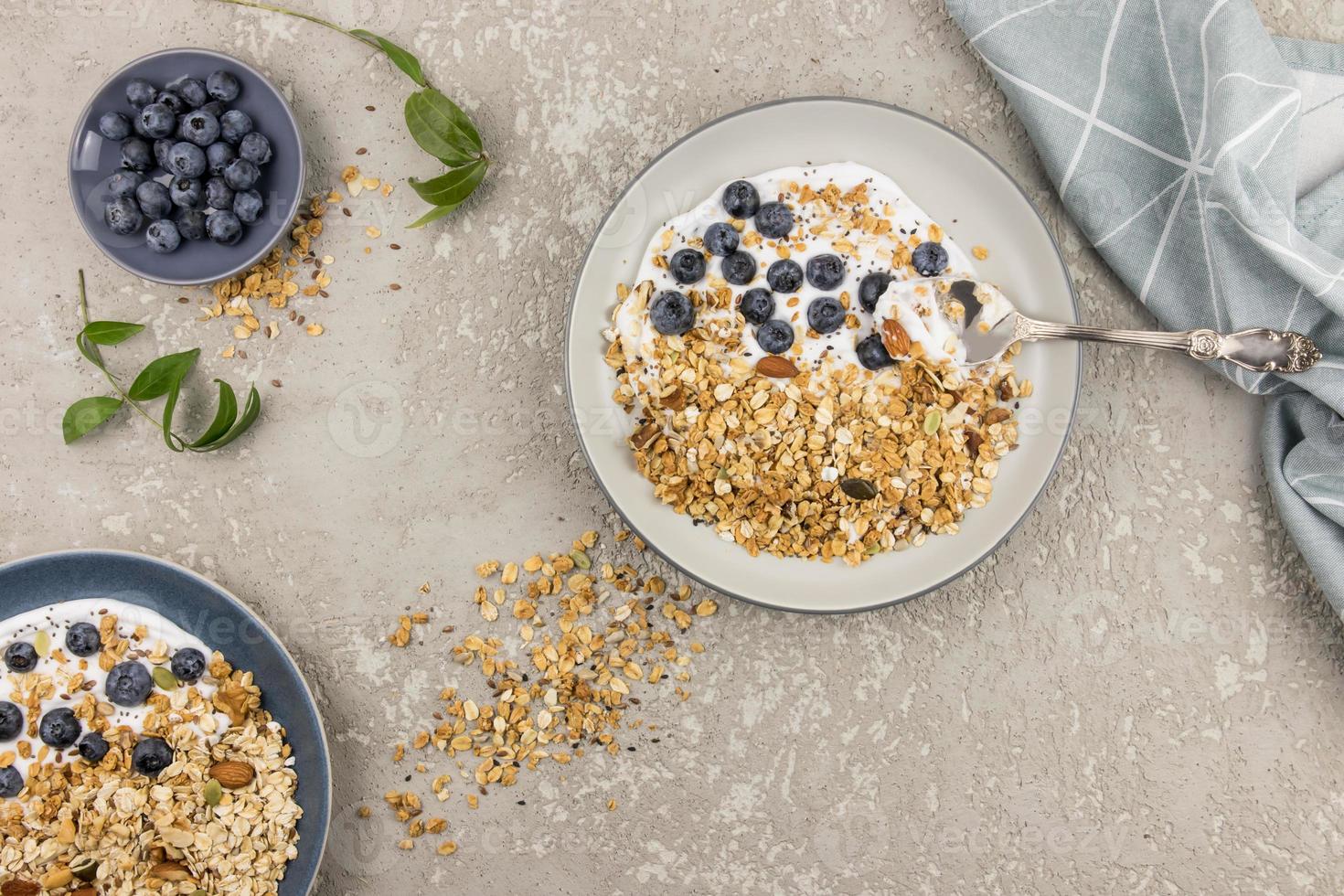 vista superior de un gran plato de granola y yogur, arándanos maduros y nueces. el concepto de una dieta sana y equilibrada. fondo de hormigón gris. foto