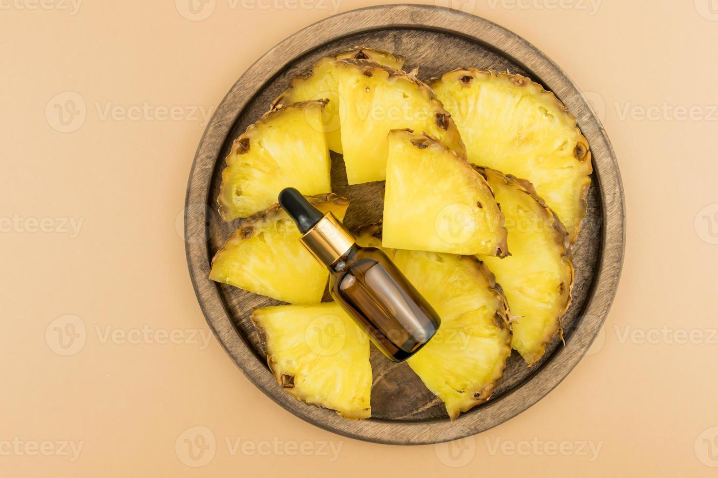 serum for facial skin care with pineapple extract lies on ripe pineapple slices and a wooden tray. top view. brown background. photo