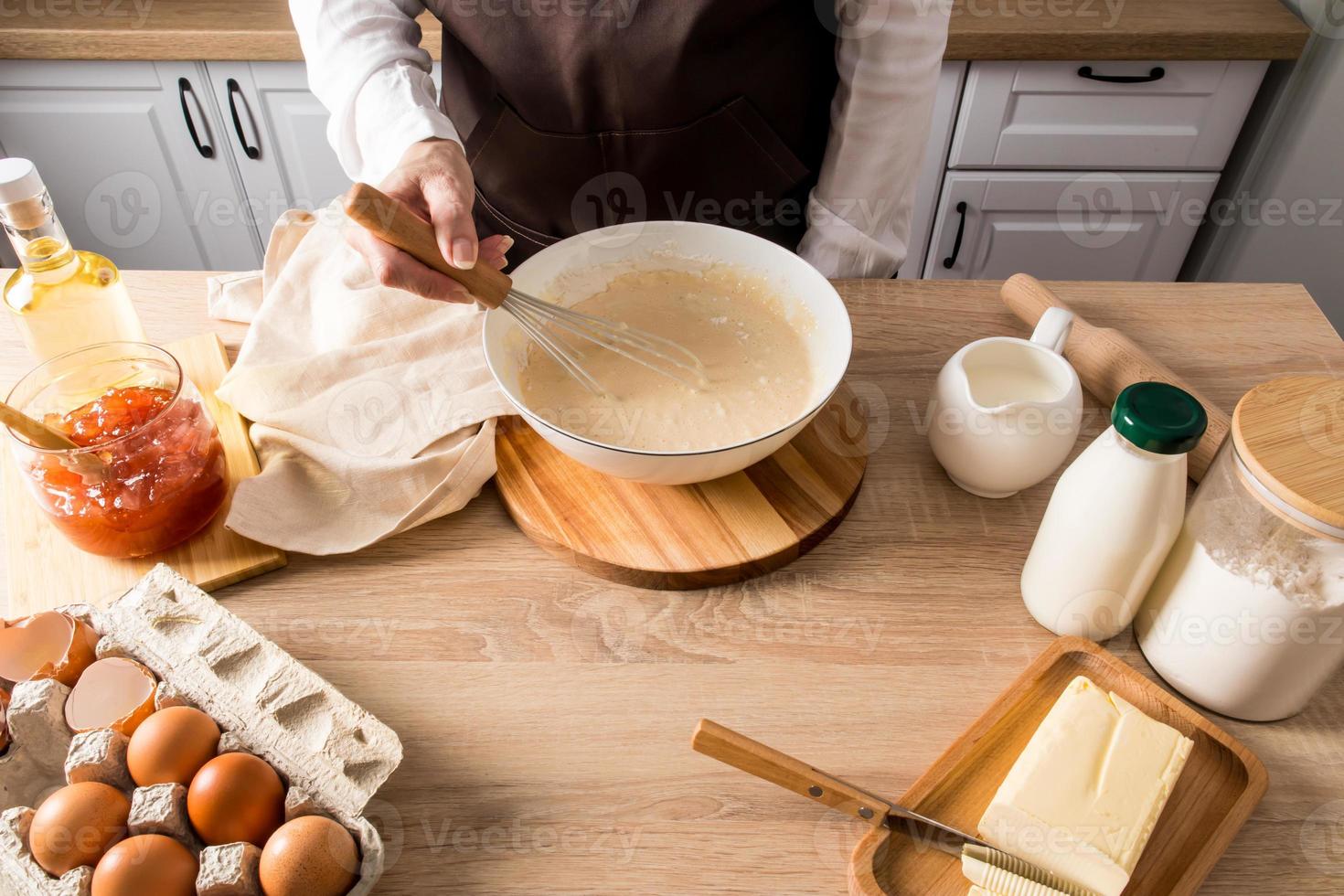 the process of preparing breakfast in the kitchen. kneading the dough in a bowl by the housewife in the headlamp. kitchen countertop with products. photo