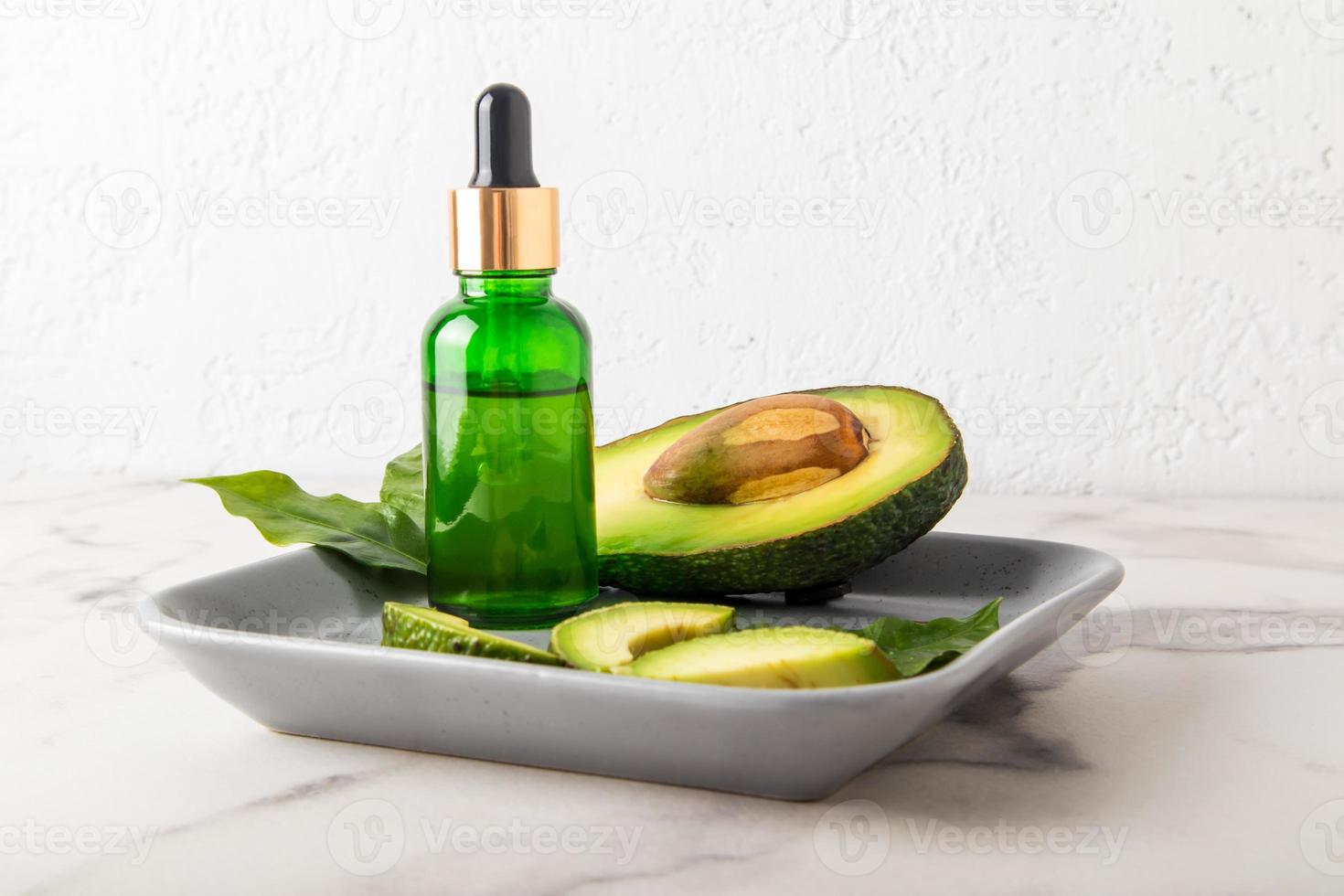 cosmetic avocado oil in a glass green bottle with a pipette on a ceramic gray tray with ripe avocado. natural cosmetics. photo