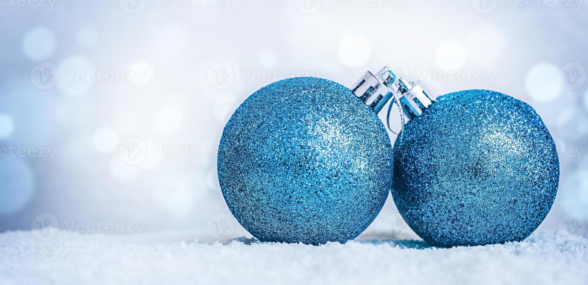 dos adornos navideños azules en la nieve sobre un fondo azul desenfocado con bokeh y espacio para copiar. foto