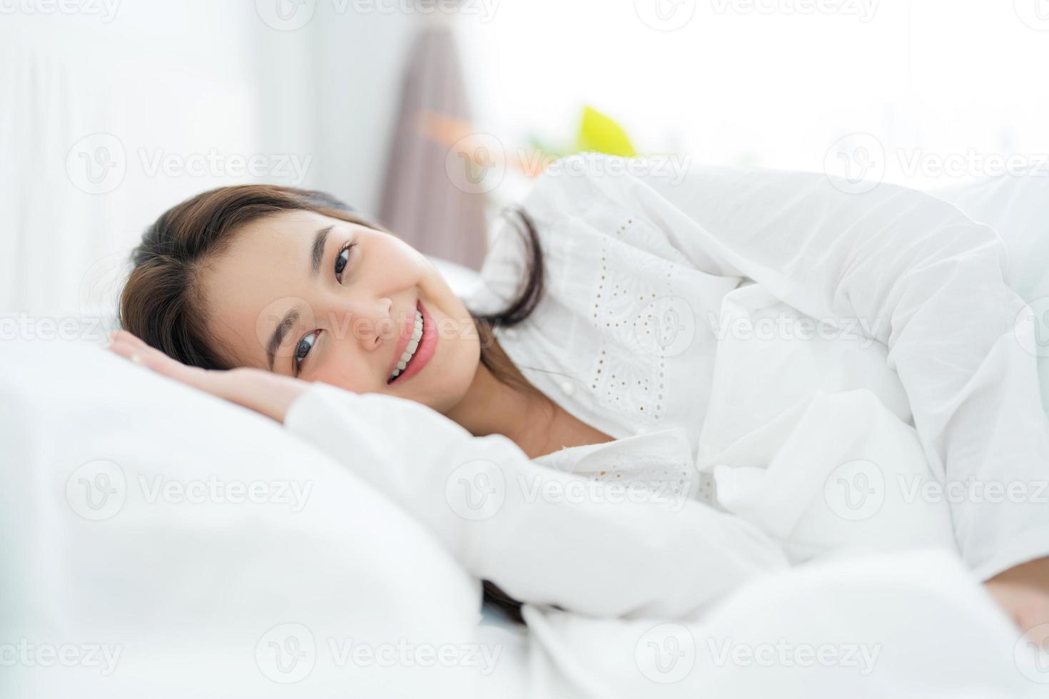 hermosa mujer asiática acostada en la cama con almohadas cómodamente apoyadas. y sonriendo felizmente foto