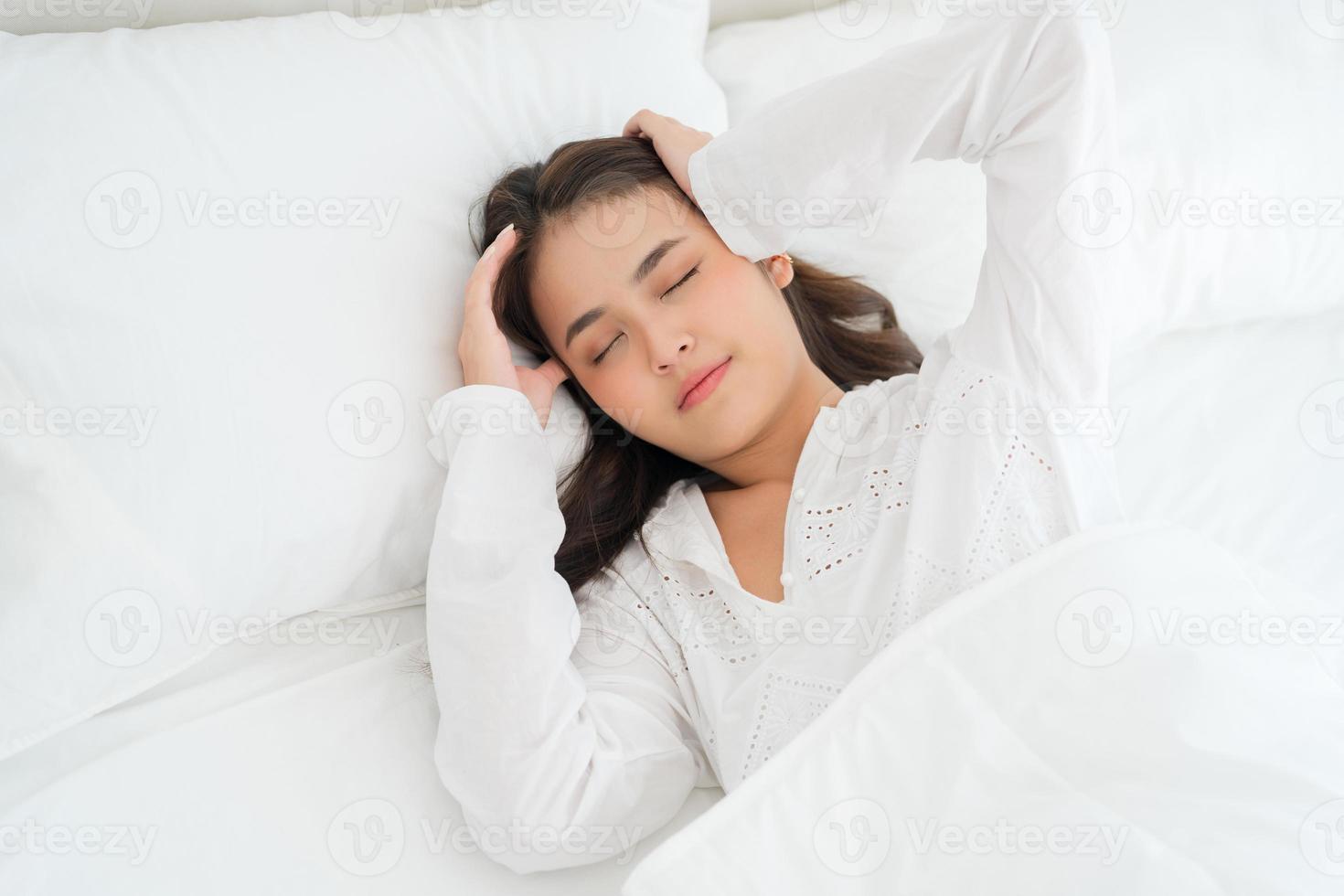 niña acostada en la cama enferma sufre de insomnio dolor de cabeza ansiedad, sosteniendo la cabeza foto