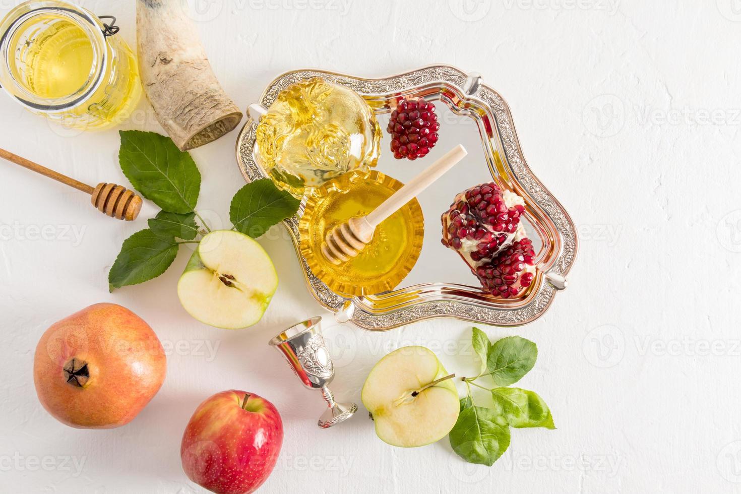 top view of a silver tray with a bowl of honey and pomegranate and ripe apples on a white background. New Year Holiday Rosh Hashanah. photo