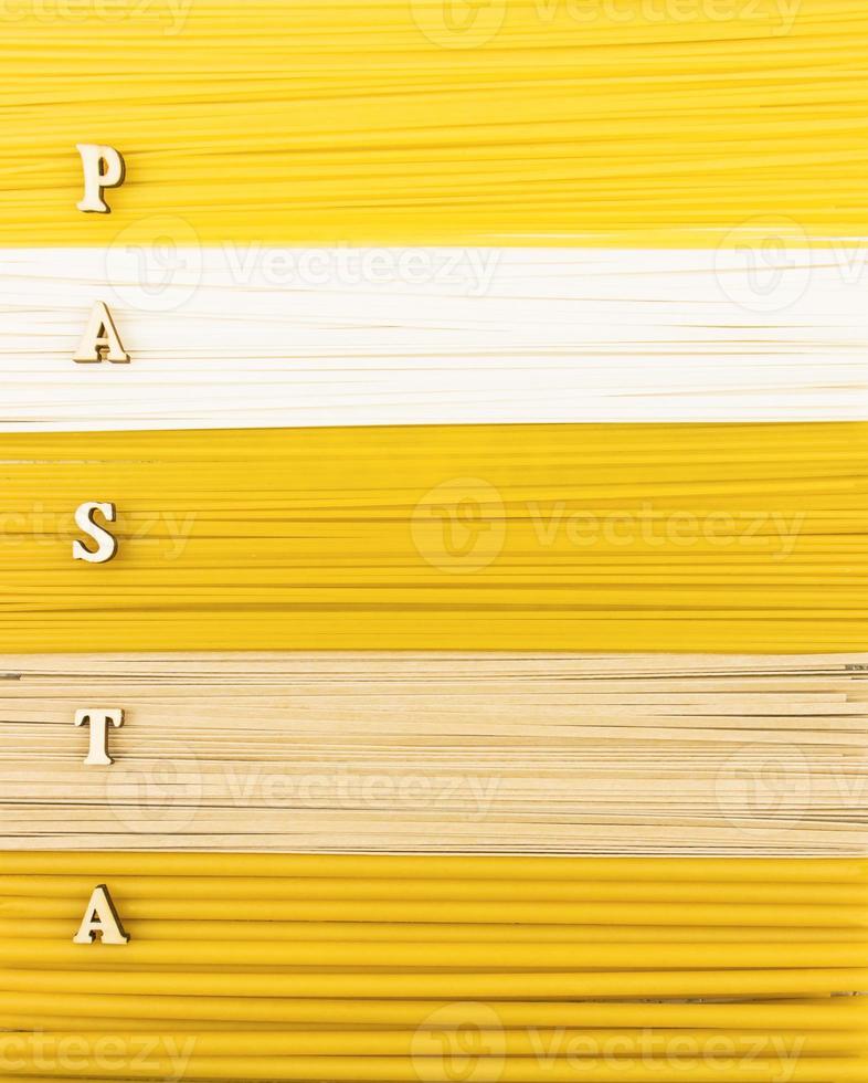 a background of dry long pasta, noodles and spaghetti with a word of wooden letter- pasta. top view. flat lay. photo