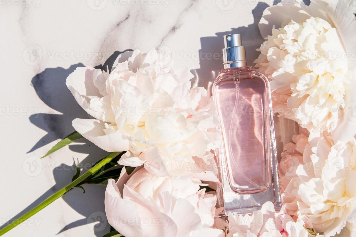 una botella de perfume de mujer con una fragancia floral entre la delicada peonía sobre un fondo de mármol. el concepto de perfumería y belleza. vista superior. foto