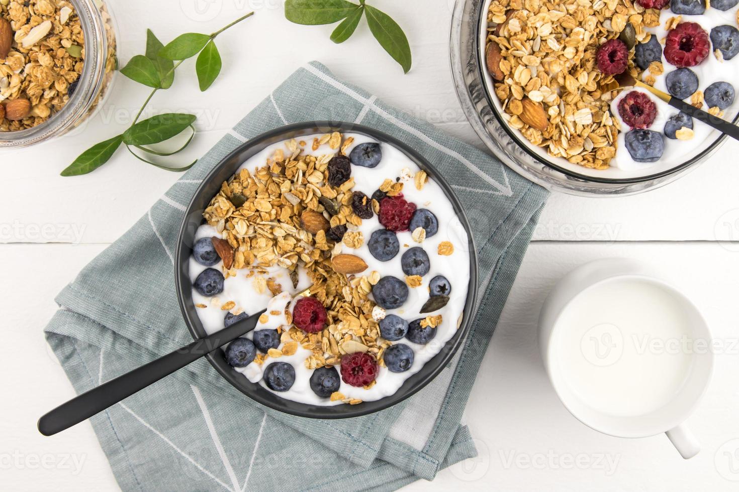 desayuno de muesli y arándanos frescos y frambuesas con yogur en tazones sobre una mesa de madera blanca. vista superior. concepto de alimentación saludable. foto