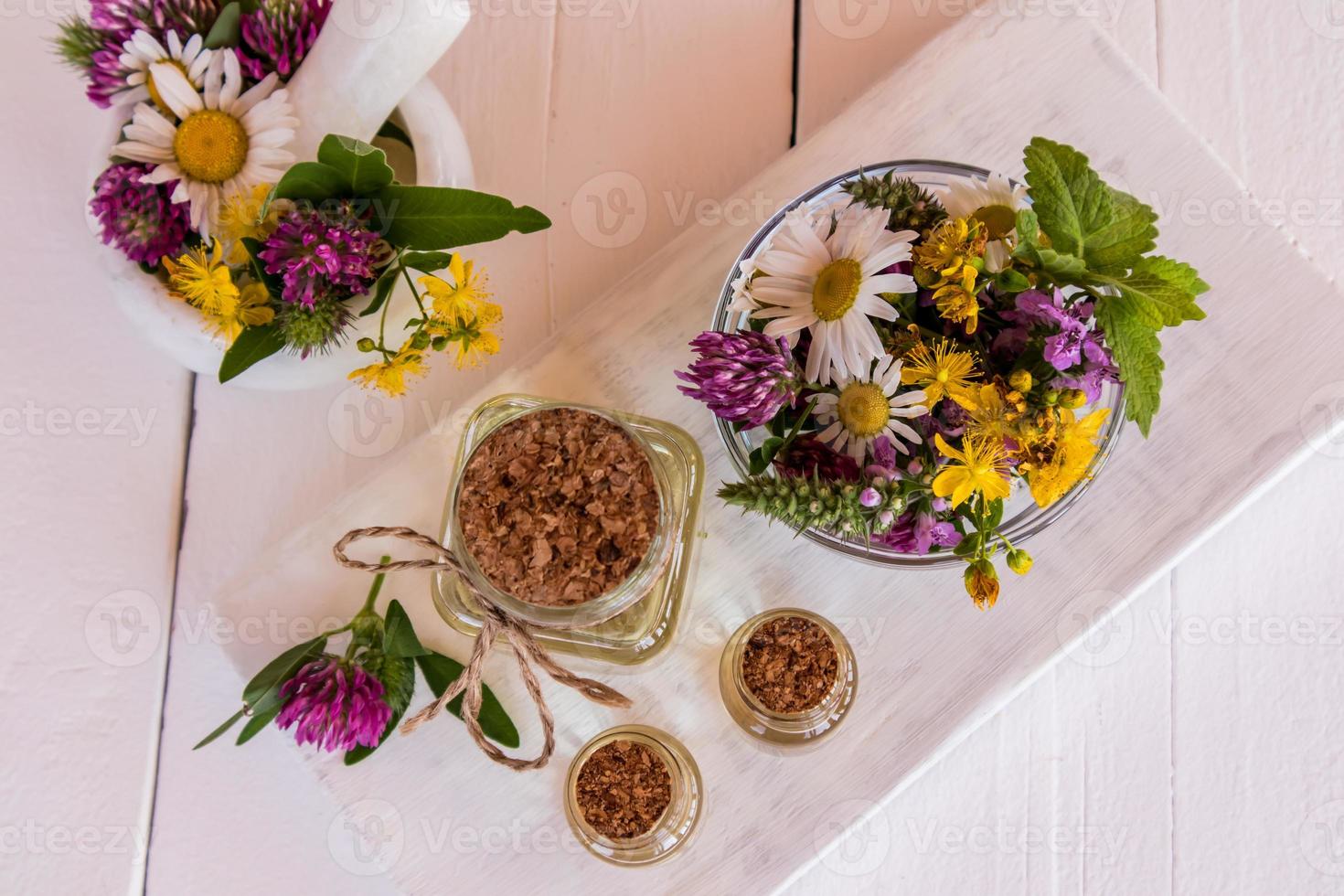glass bottles of organic St. John's wort oil stand on a table of white wooden boards. mortar and pestle with grass flowers. alternative medicine. photo