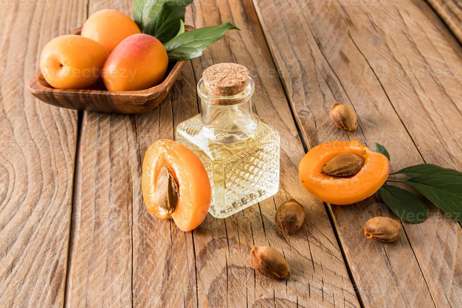 apricot oil in glass bottle on the background of ripe apricots and seeds. wooden background. the concept of rejuvenation, moisturizing the skin. photo