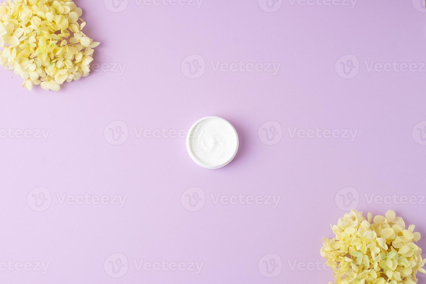 Jar of cosmetic cream with flowers on rose background. Flat lay, copy space photo