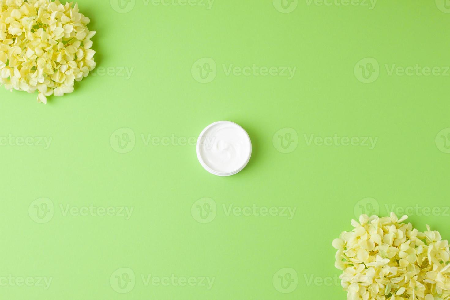 Jar of cosmetic cream with flowers on green background. Flat lay, copy space photo