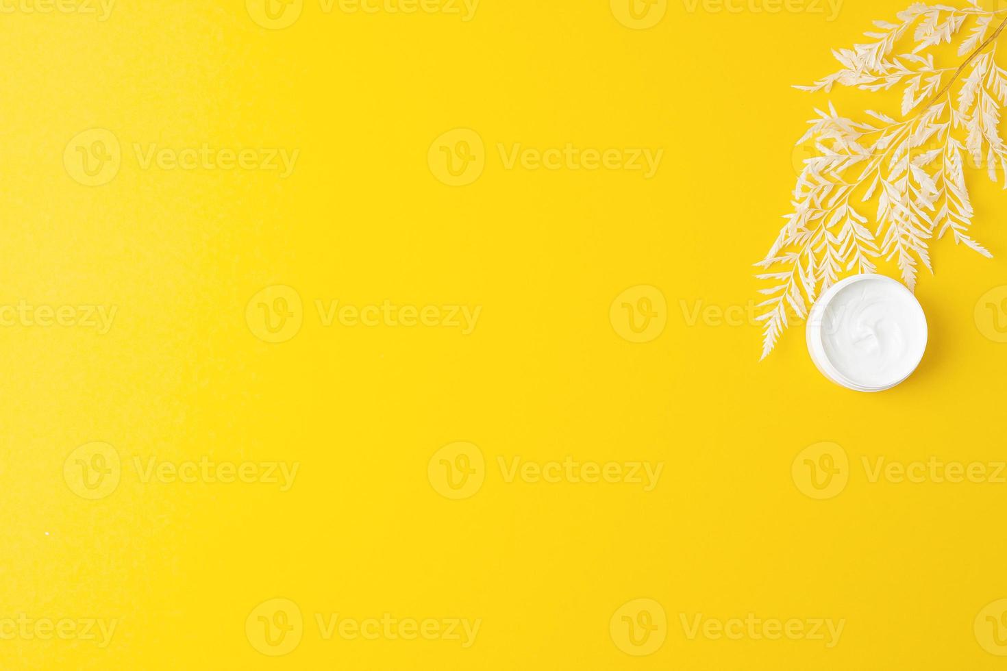 Jar of cosmetic cream with flowers on yellow background. Flat lay, copy space photo