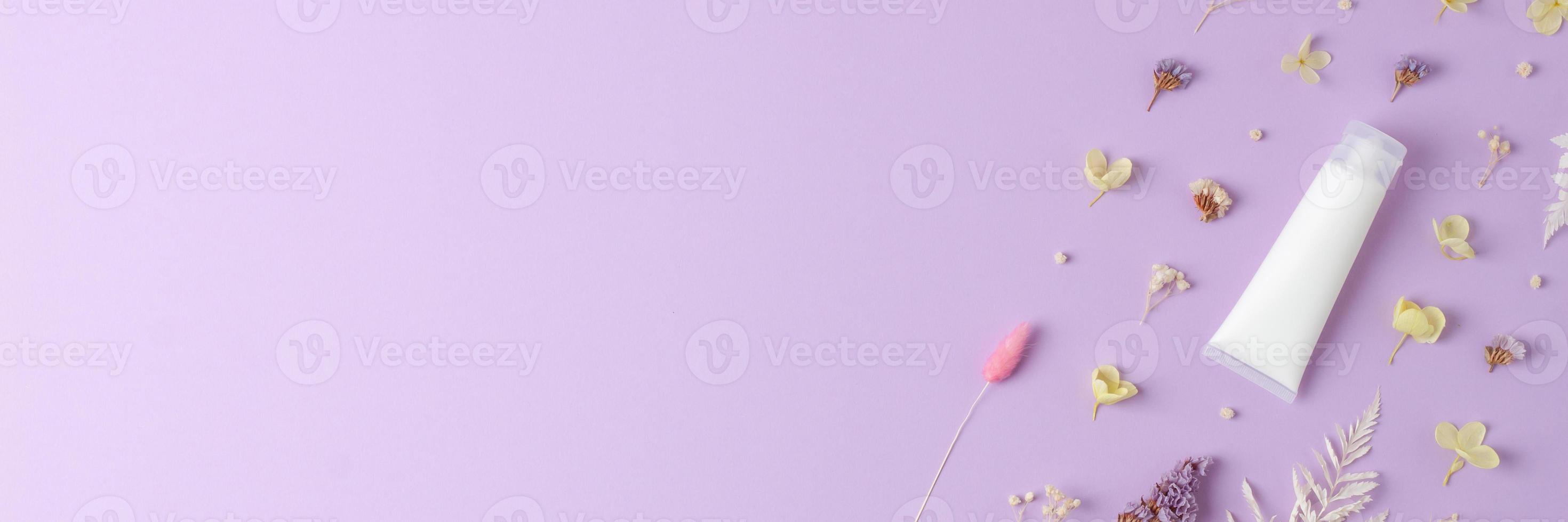 White tube of cosmetic cream with flowers on rose background. Flat lay, copy space photo