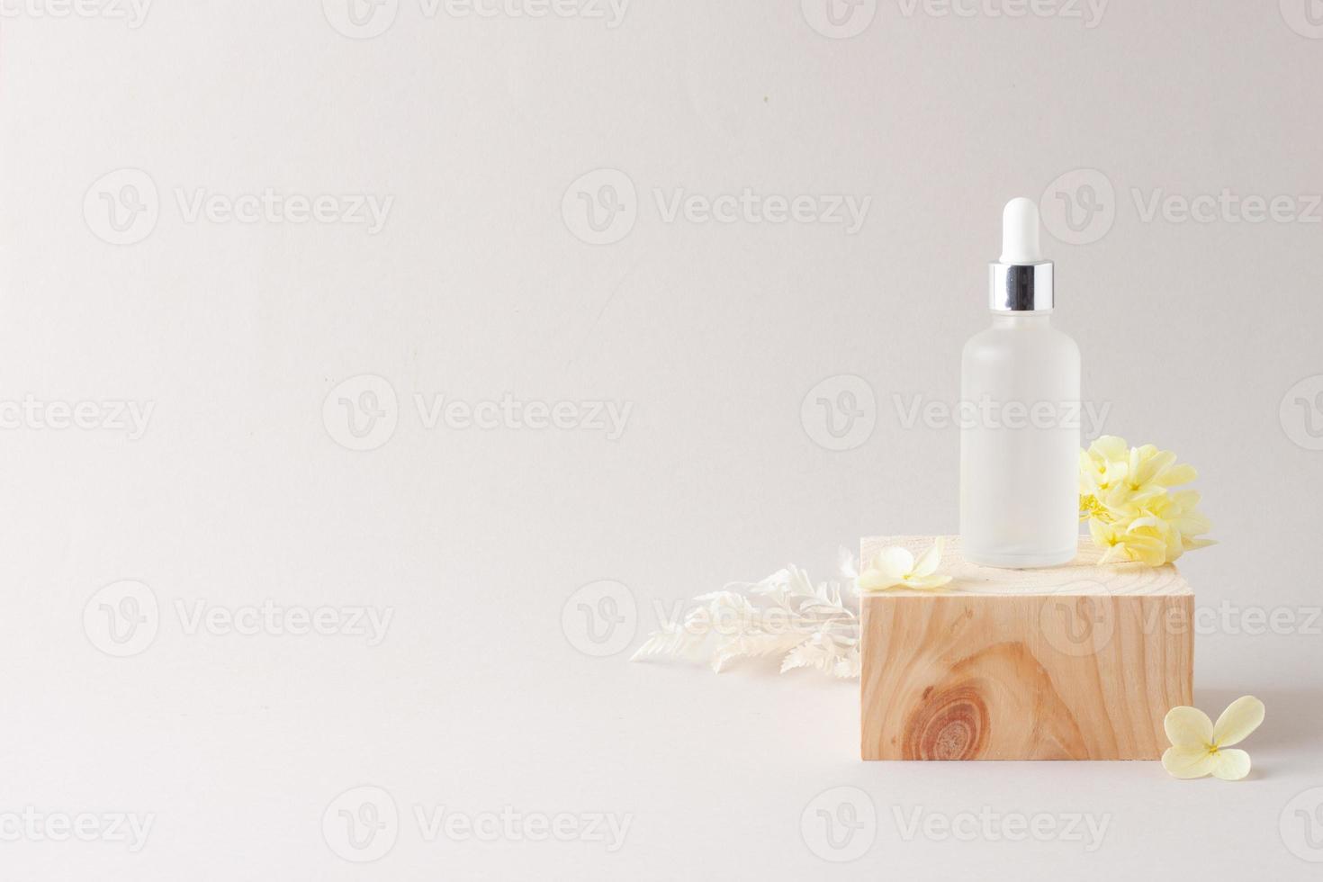 Cosmetic bottle with wood podium and flowers on grey background. Close up, copy space photo