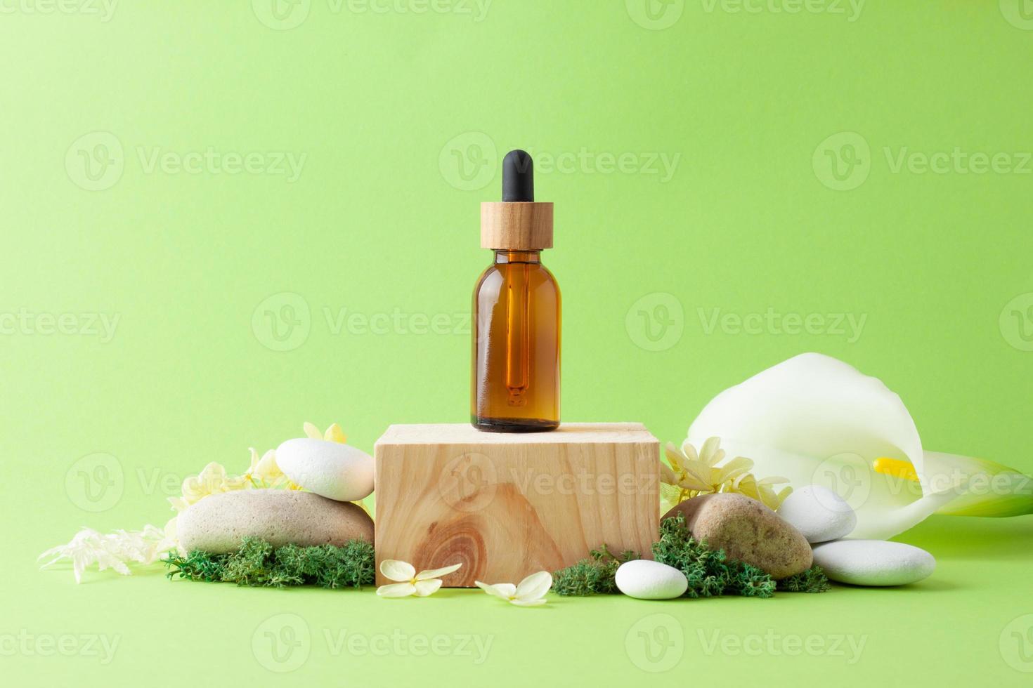 Cosmetic bottle with wood podium and flowers, moss, stone on green background. Close up, copy space photo