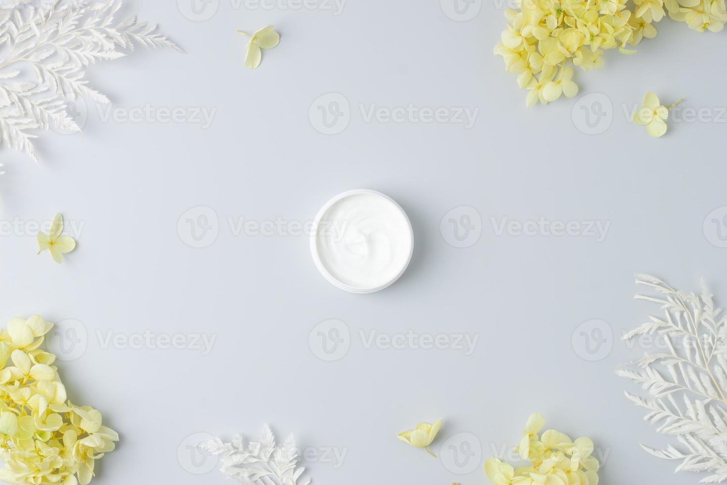 Jar of cosmetic cream with flowers on grey background. Flat lay, copy space photo