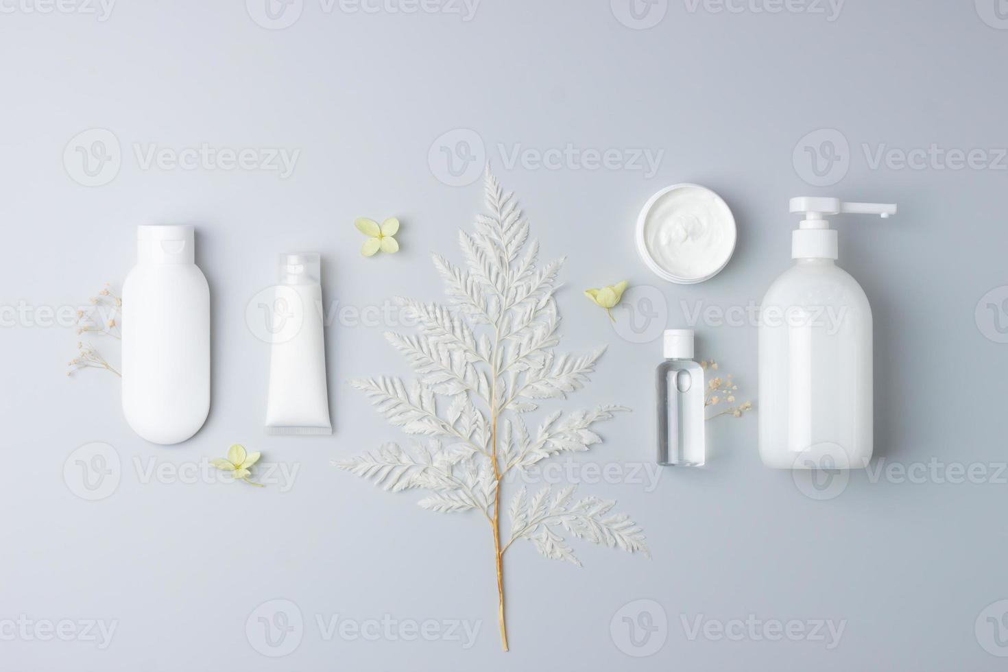 Cosmetic composition with cosmetic skin care products and flowers on grey background. Flat lay, copy space photo