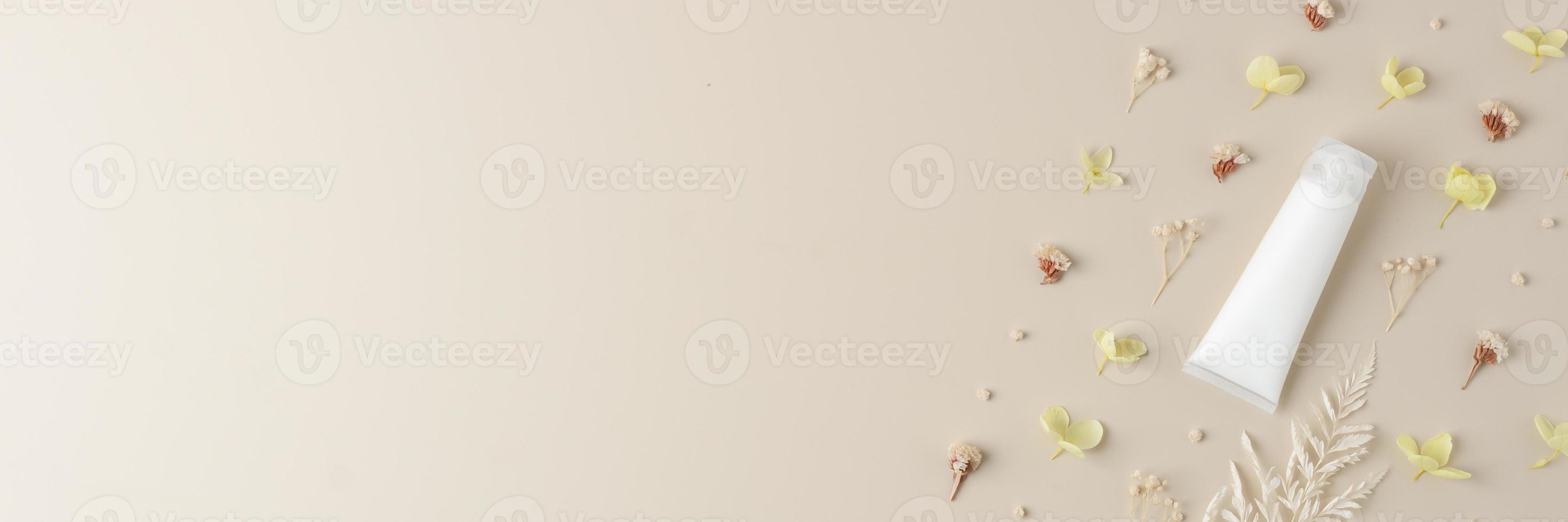 White tube of cosmetic cream with flowers on pastel beige background. Flat lay, copy space photo