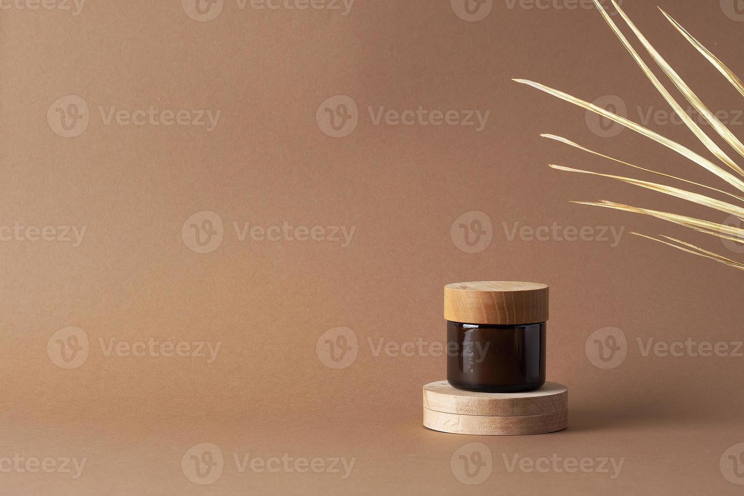 Jar of cosmetic cream with wood podium and palm leaf on brown background. Close up, copy space photo