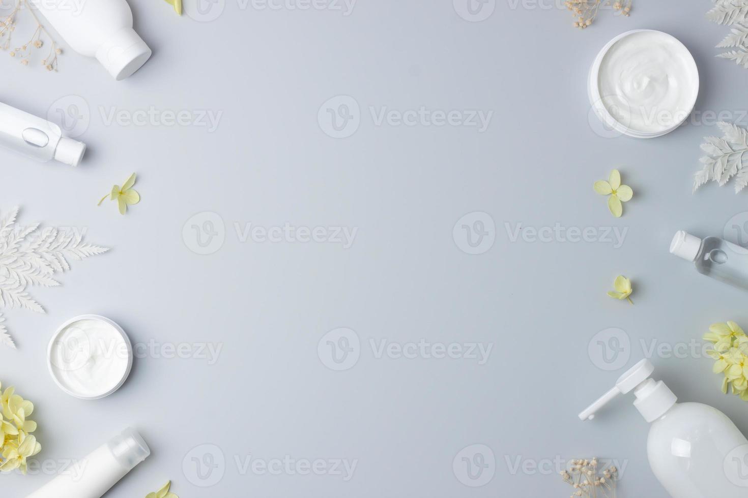 Cosmetic skin care products with with flowers on grey background. Flat lay, copy space photo