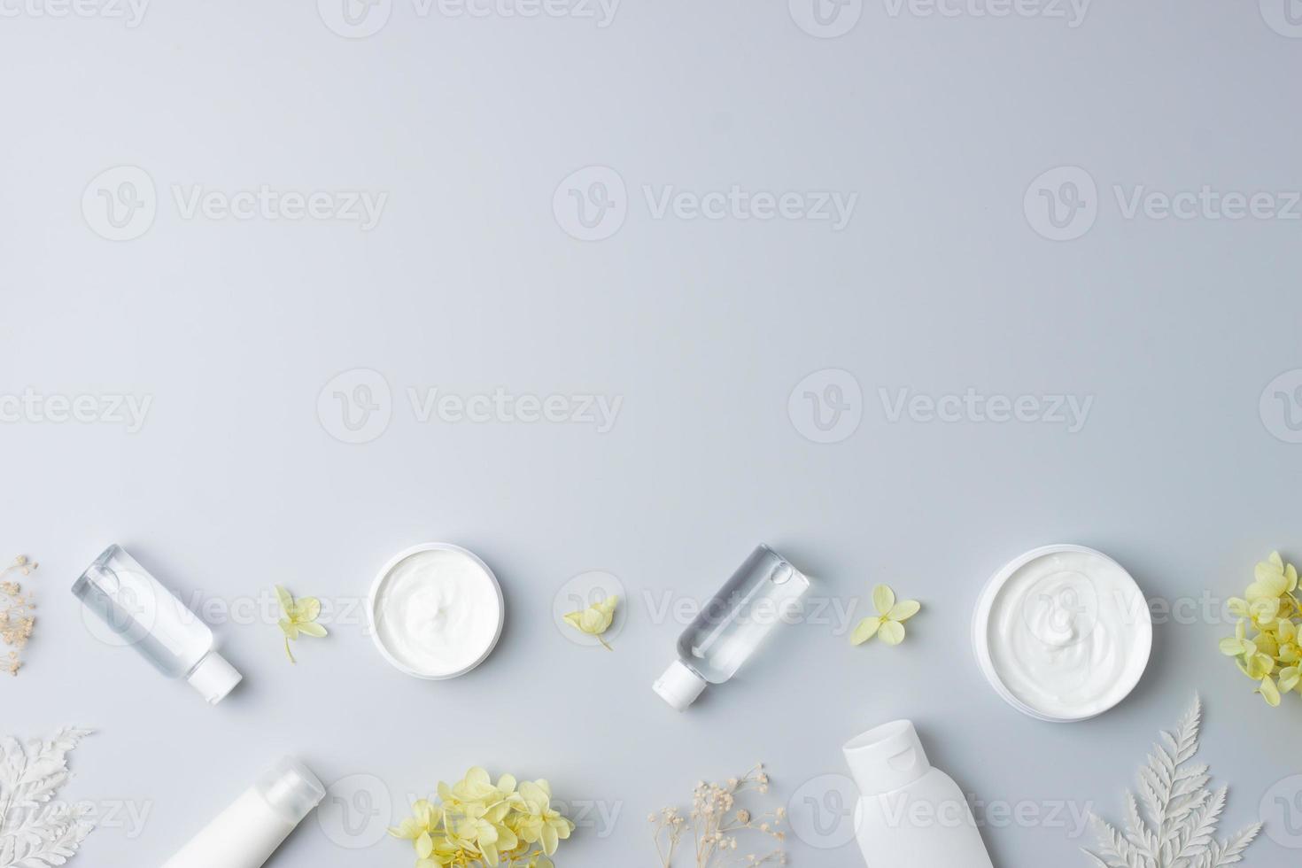 productos cosméticos para el cuidado de la piel con flores sobre fondo gris. endecha plana, espacio de copia foto