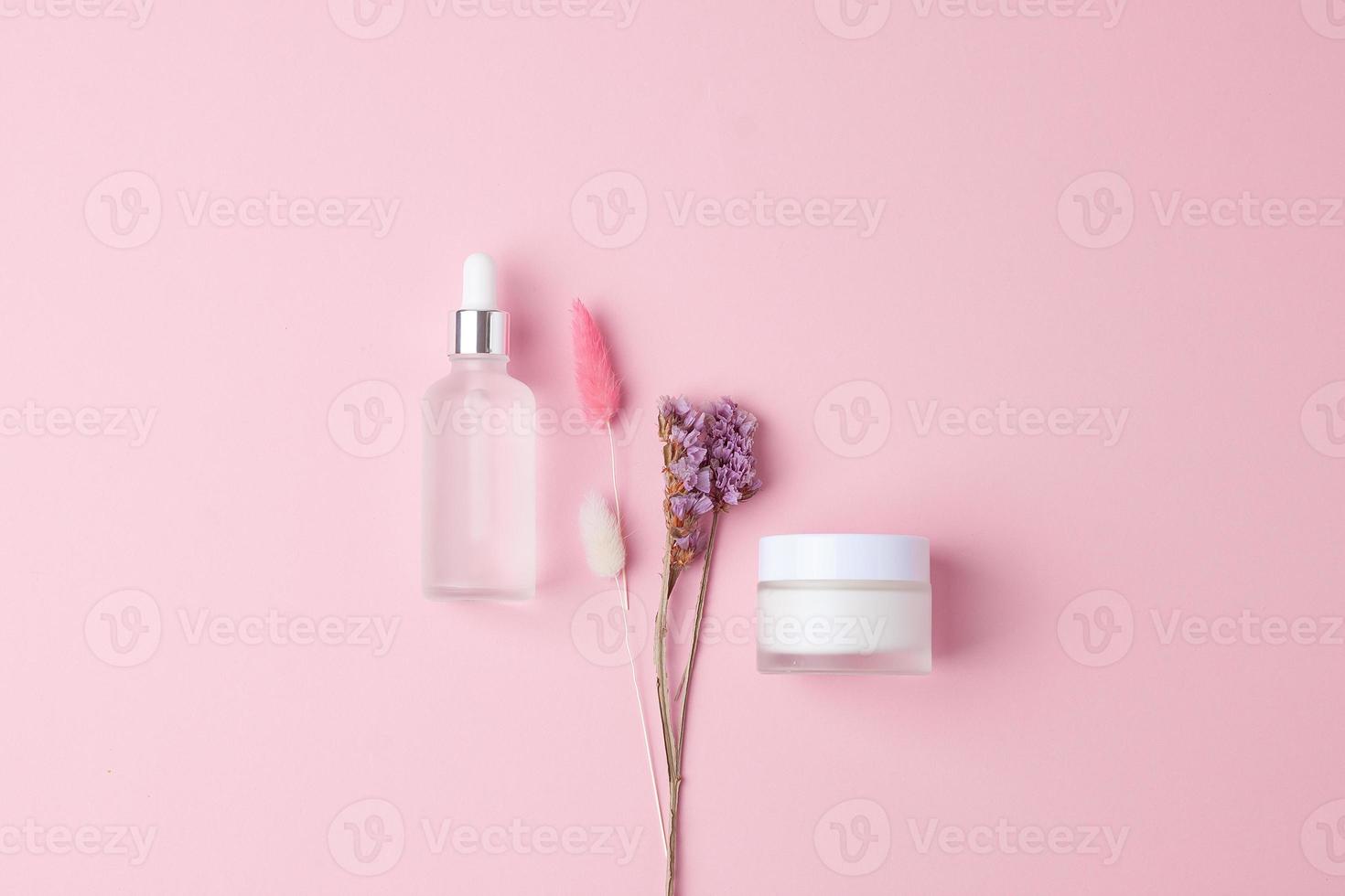 composición mínima con productos cosméticos para el cuidado de la piel y flores sobre fondo rosa. endecha plana foto