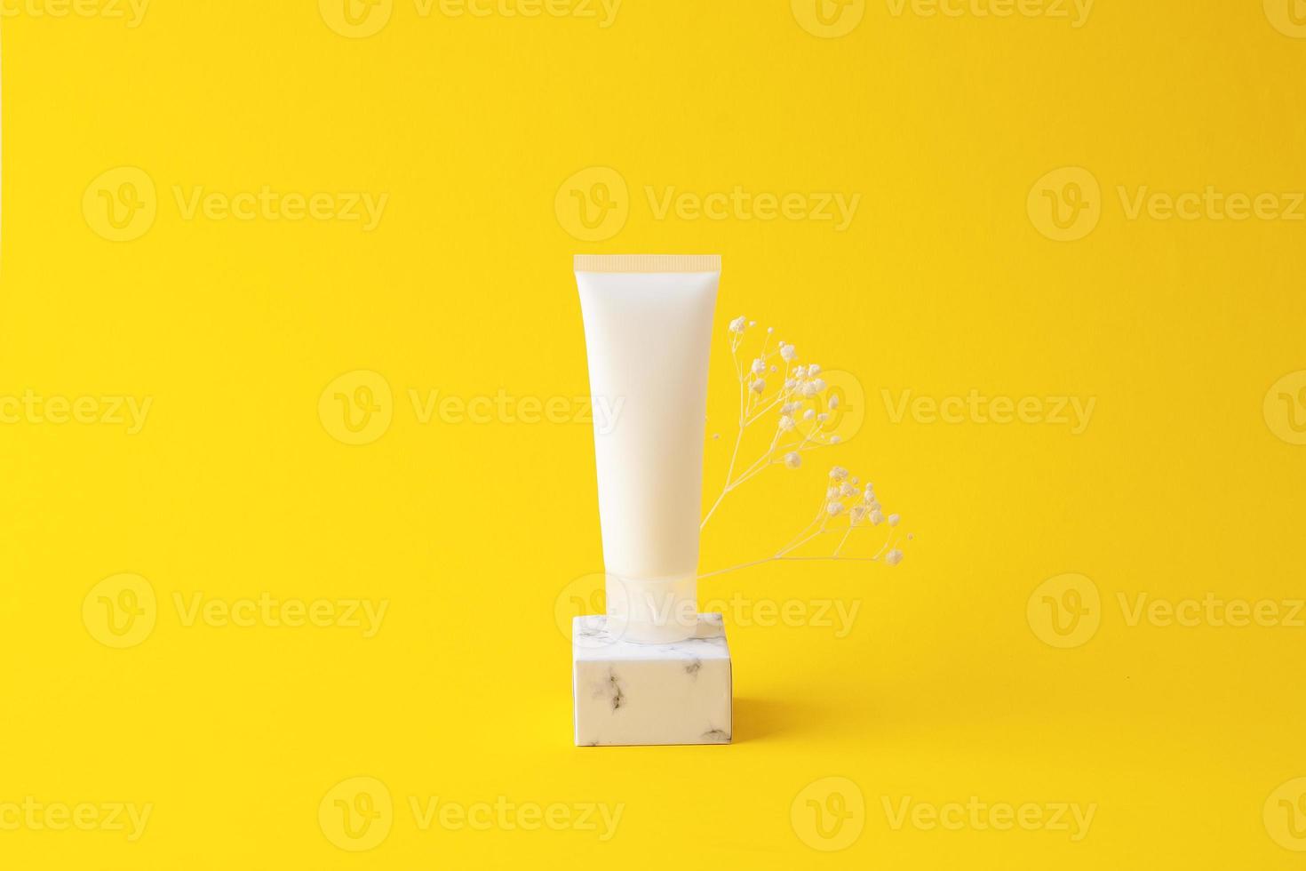 White tube of cosmetic cream on podium on yellow background. Close up. photo