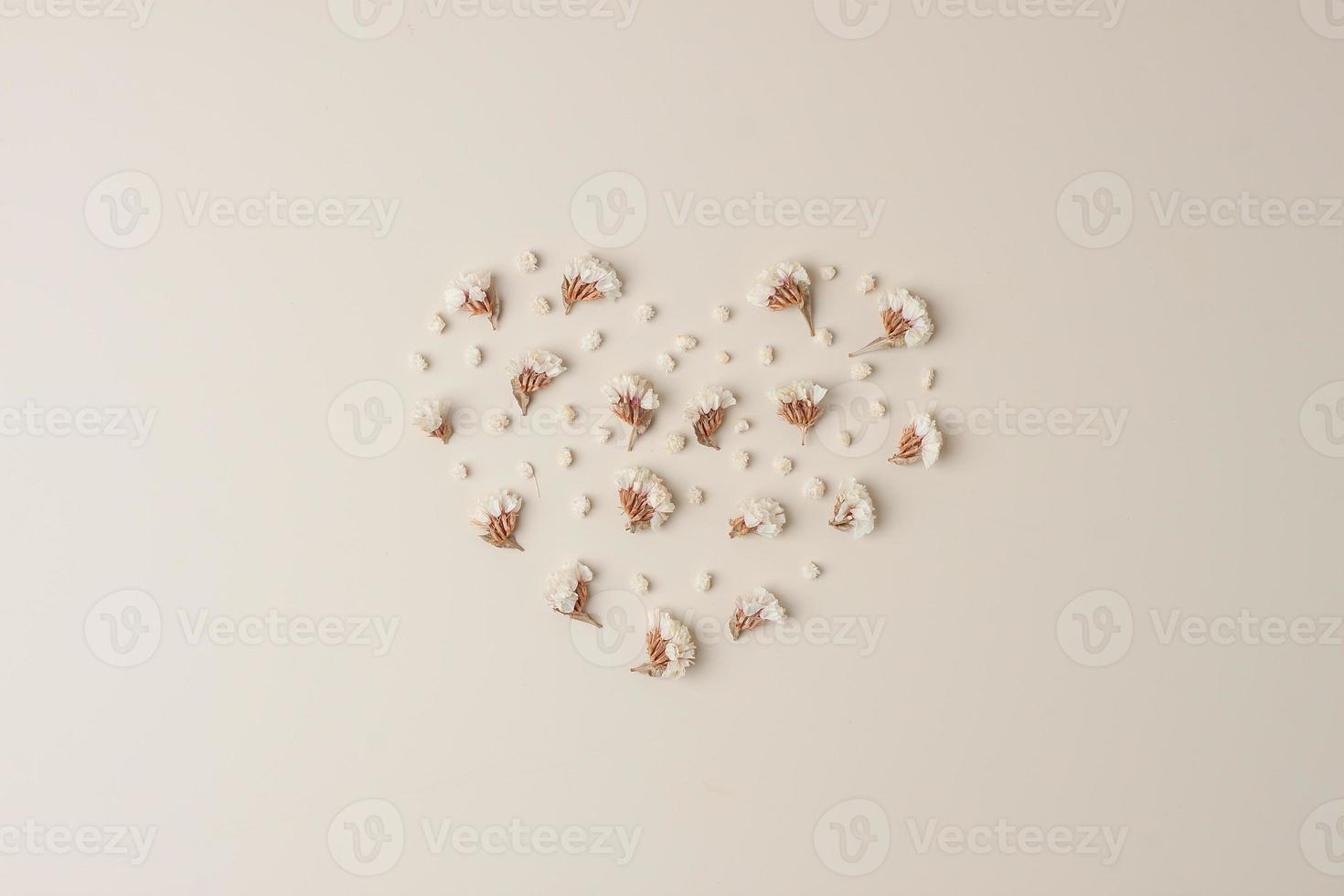 Minimal composition with a heart shape of flowers on pastel beige background. Flat lay, copy space photo