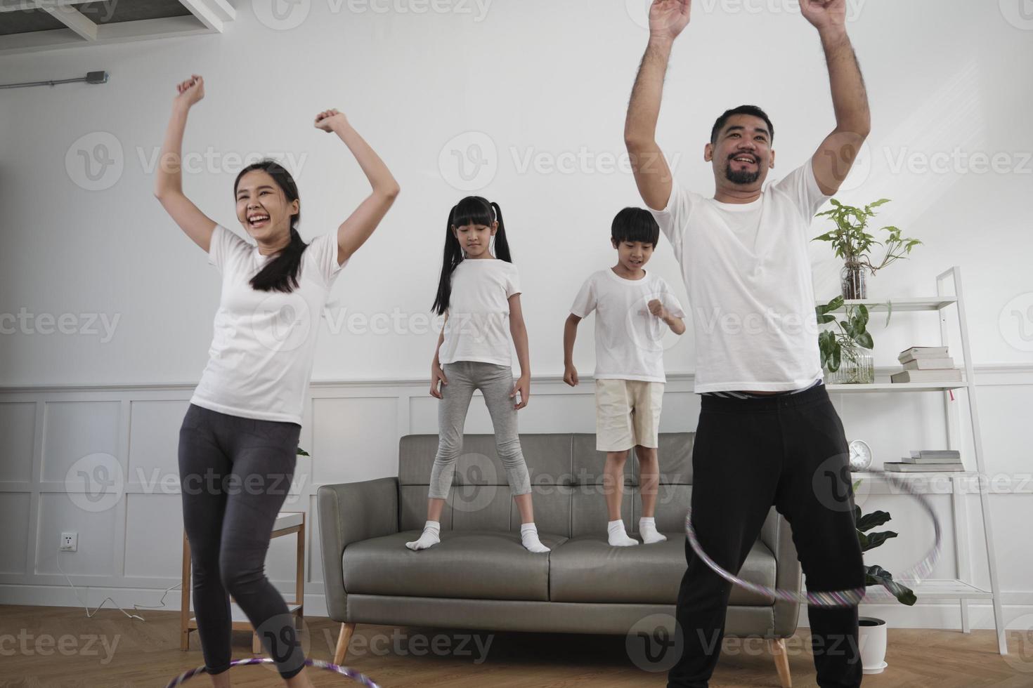 feliz bienestar familia tailandesa asiática, padres e hijos son divertidos jugando hula hoops juntos, entrenamiento físico y ejercicio saludable en la sala de estar blanca, el estilo de vida doméstico y la actividad de fin de semana. foto